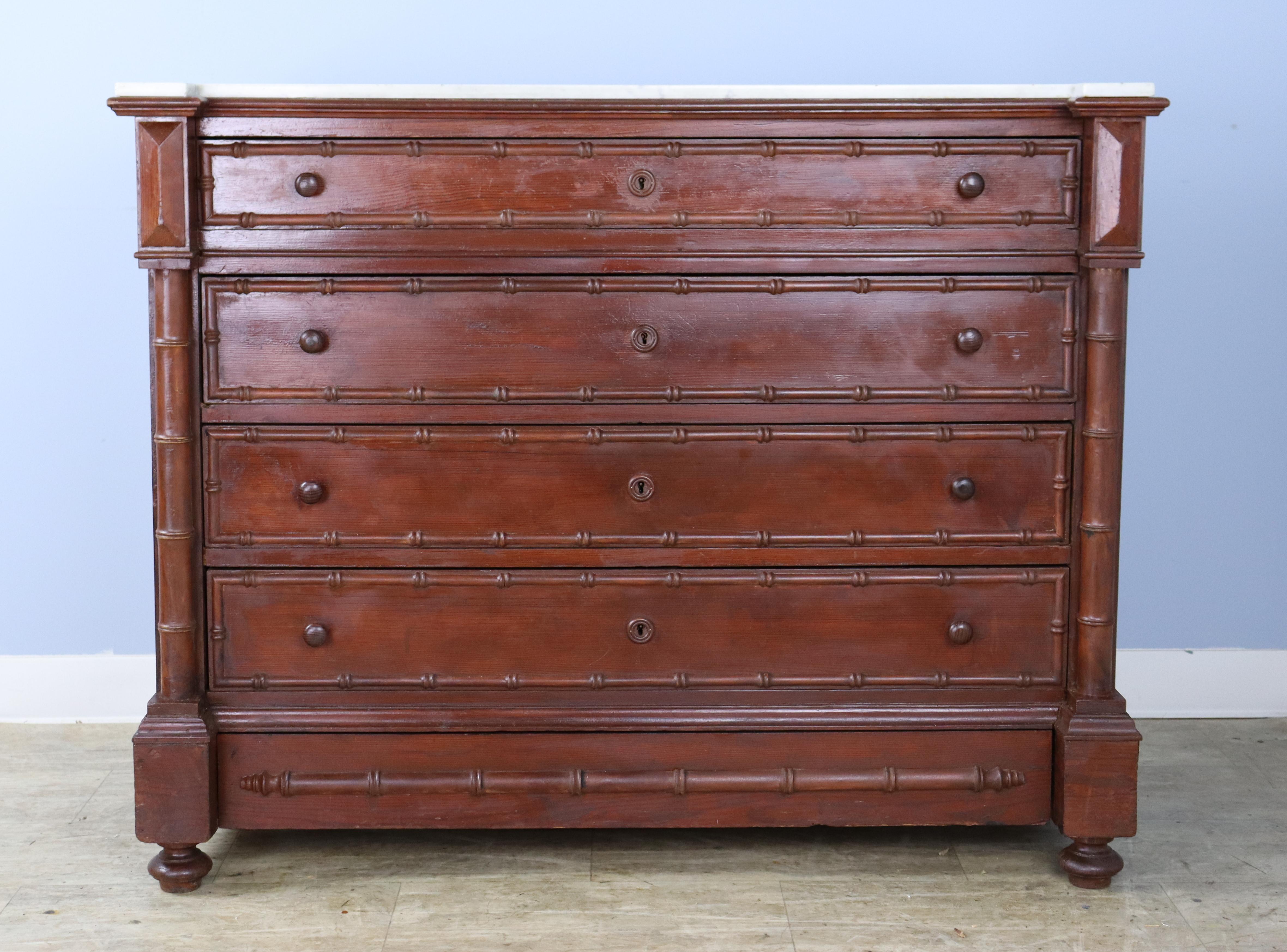 A charming dark pine chest of drawers with faux bamboo columns and mouldings. Slightly unusual construction with top detail and a hidden fifth drawer at the bottom. The marble which is original is fine antique condition, with the exception of some