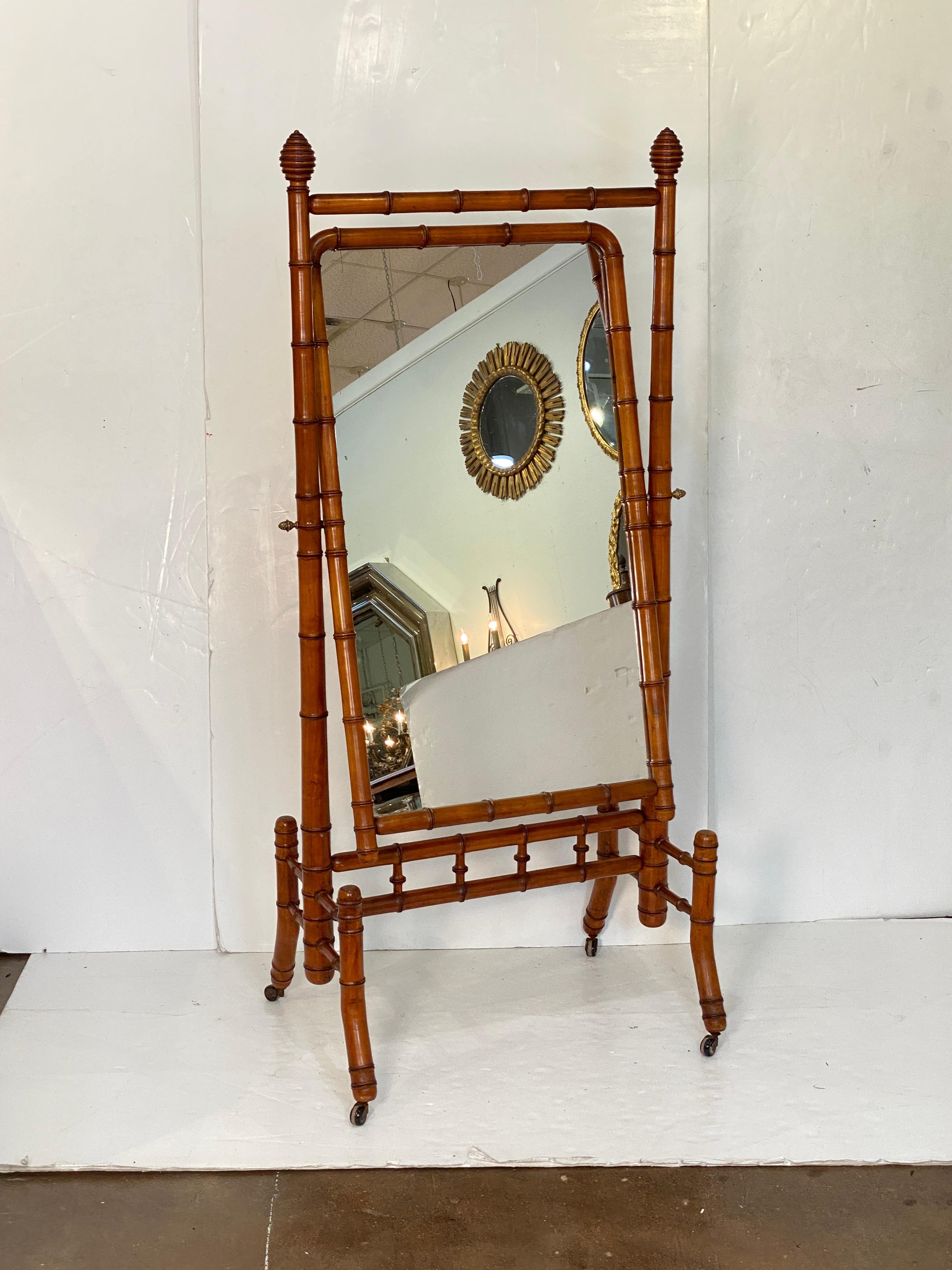 A fine large French faux bamboo cheval or full-length dressing mirror, c.1870-1910, featuring a mirrored glass panel framed in turned wood with a bamboo design, mounted to a rolling frame of turned wood, capped with turned finials, with a stretcher