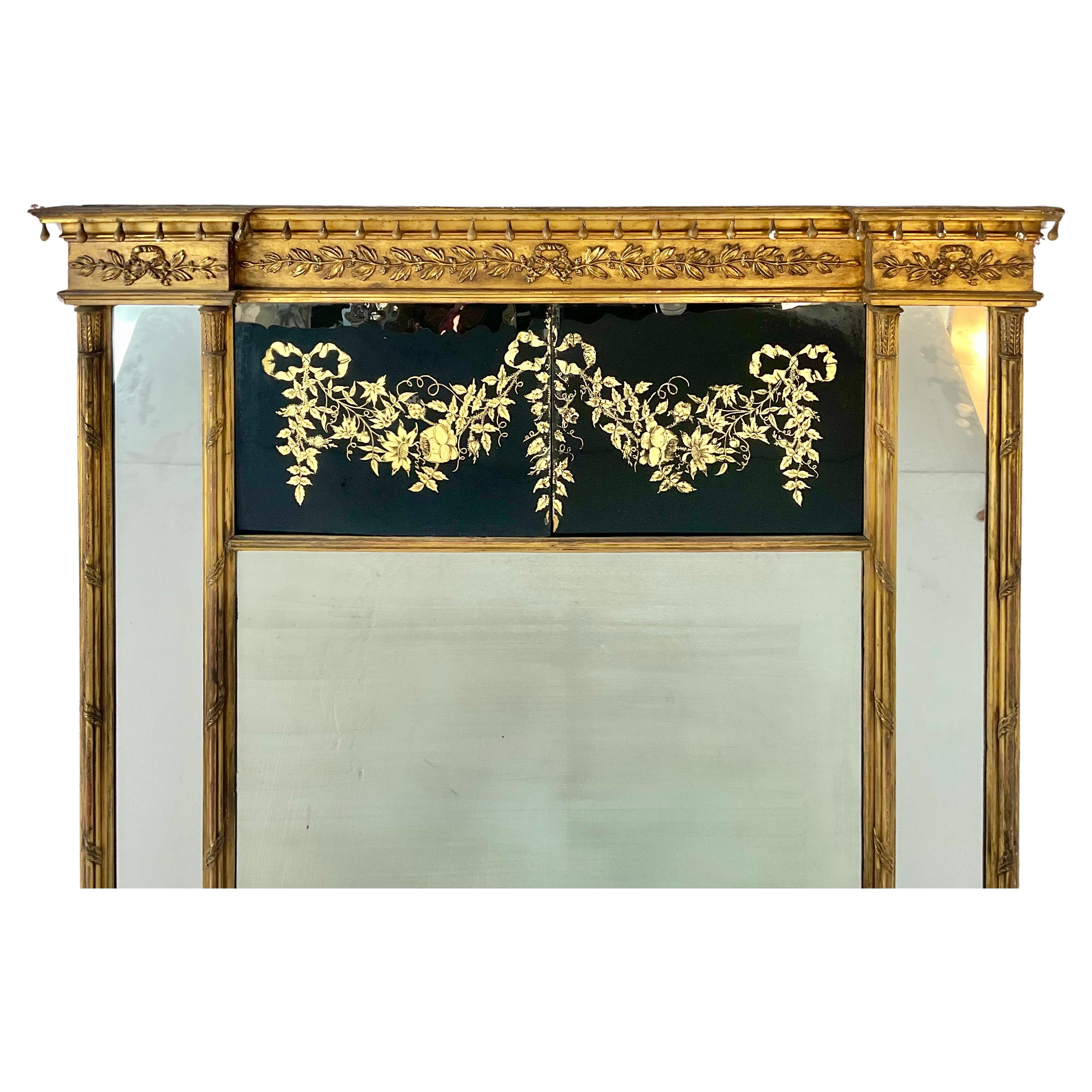 A Large and Rare Federal Carved Giltwood and Eglomise Overmantel Mirror. Mirror is flanked by double gilded columns on each side, with mirrored inserts that enhance the sense of depth and light. Frame is carved with delicate gilt foliate and ribbon
