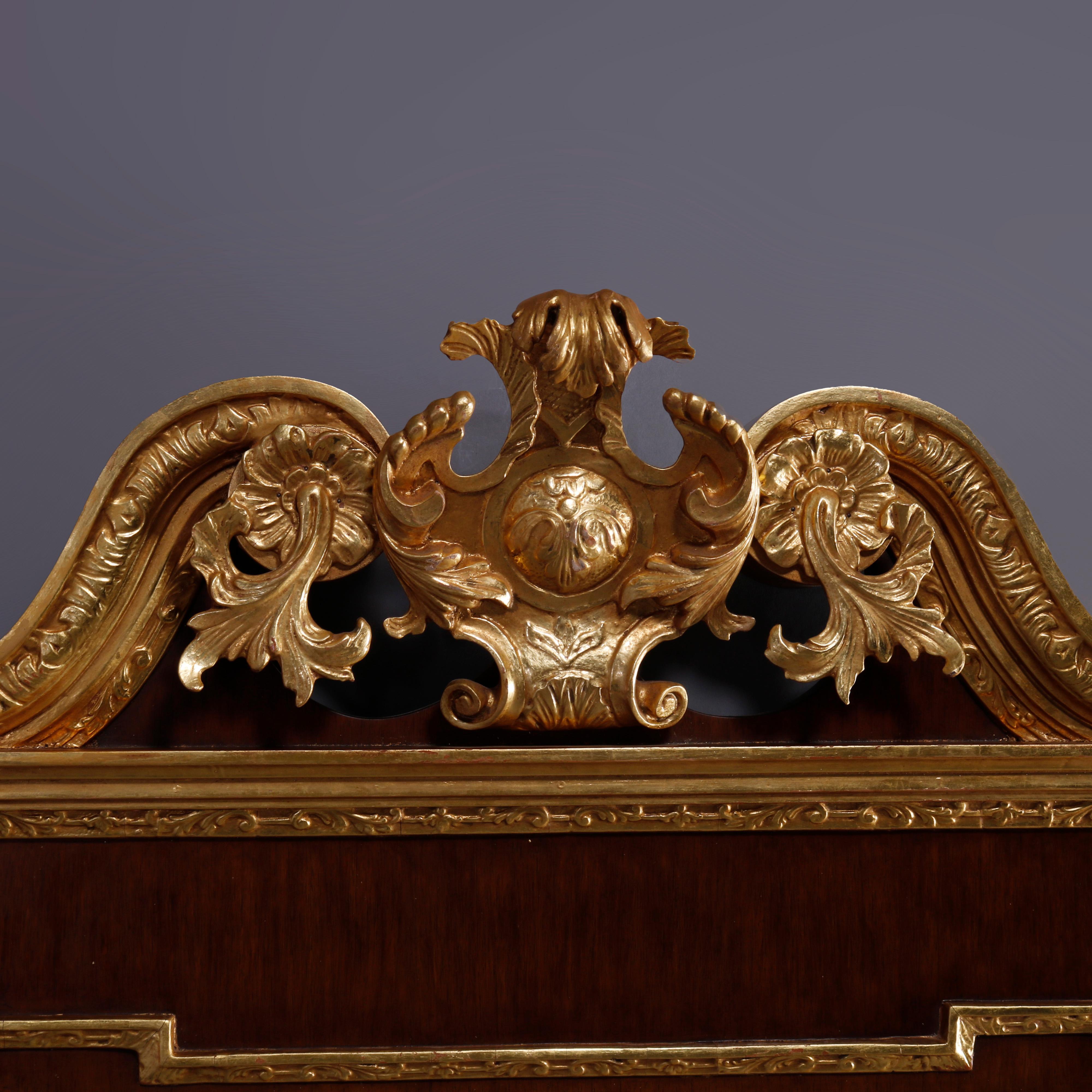 An oversized Federal style wall mirror by Kittinger in the Colonial Williamsburg line offers mahogany construction in shaped form with giltwood crest having central foliate shield cartouche with flanking gilt foliate elements, en verso label, 20th
