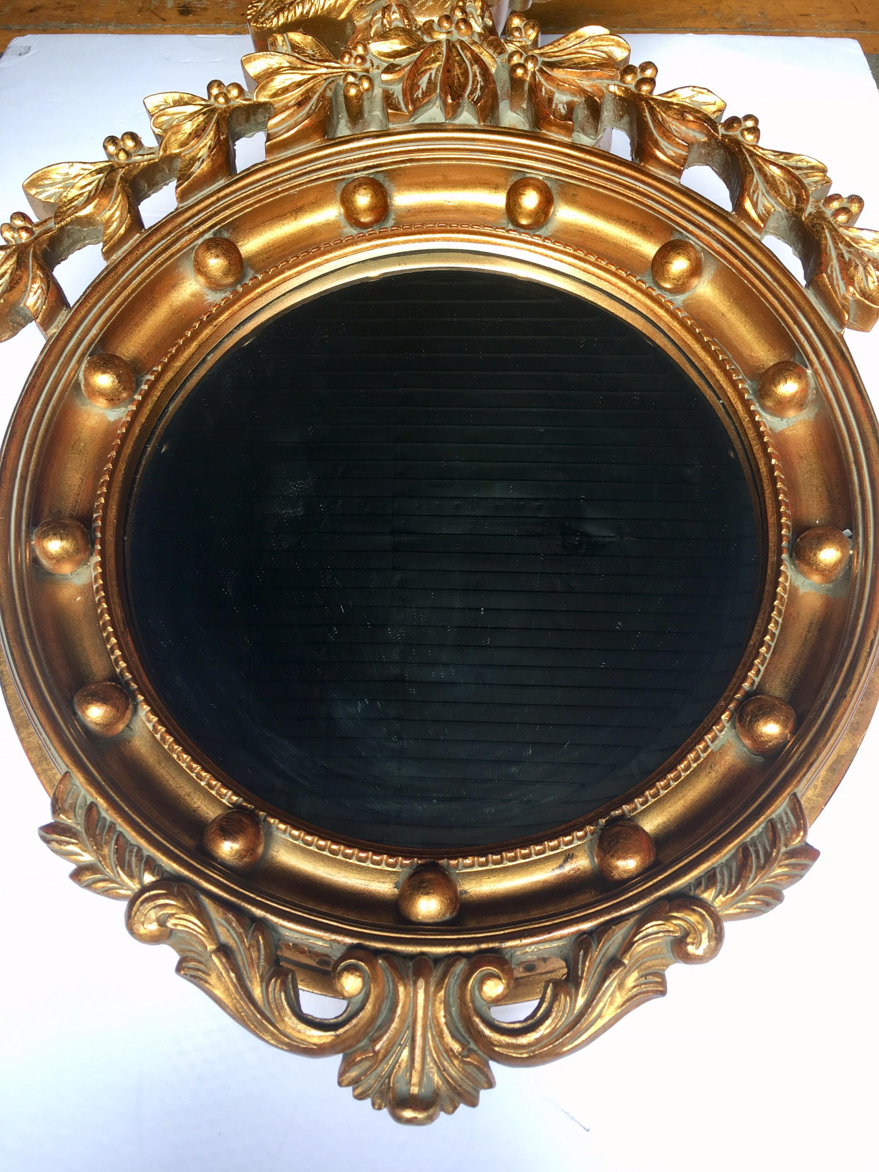 Large dimensional traditional Federal style round mirror with perched eagle flanked by acanthus surmounting. Carved-like frame is constructed of a light weight composition and is finished in a metallic gold painted finish. Beveled mirror measures 16