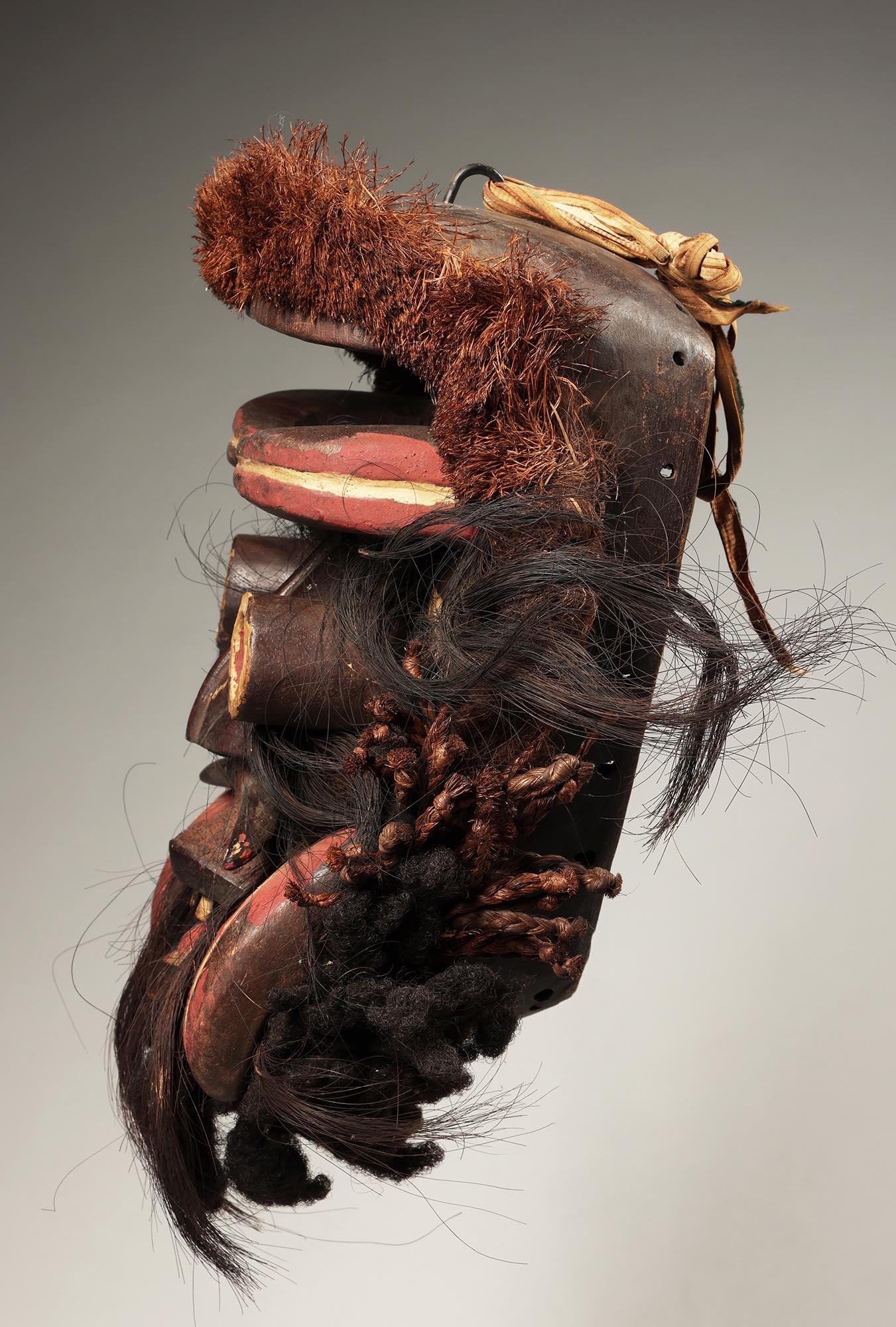 Große grimmige Dan Guere oder Wir-Maske von der Elfenbeinküste Afrika ex Fearing Sammlung. 
Kräftige Maske mit offenen, röhrenförmigen Augen, vorstehenden, geschnitzten Holzhauern, offenem Mund mit Zähnen und angebrachtem Raphia und Haar.

Es ist in