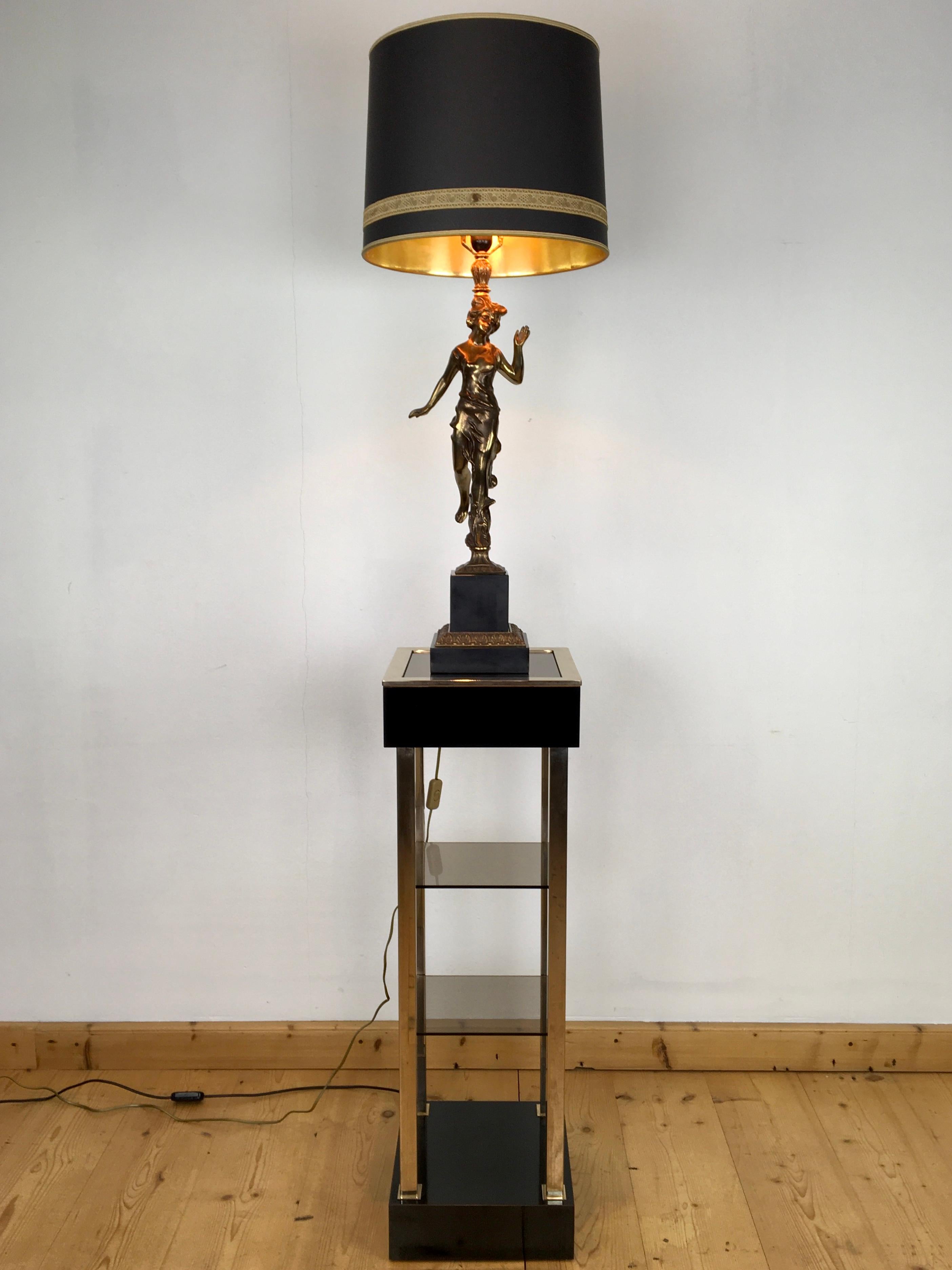Spectacular large figural table lamp with an elegant lady.
A Hollywood Regency table lamp with an Art Nouveau touch made by Deknudt Belgium.
A graceful lady or women in draped dress standing on one foot on a Belgian black marble base which has