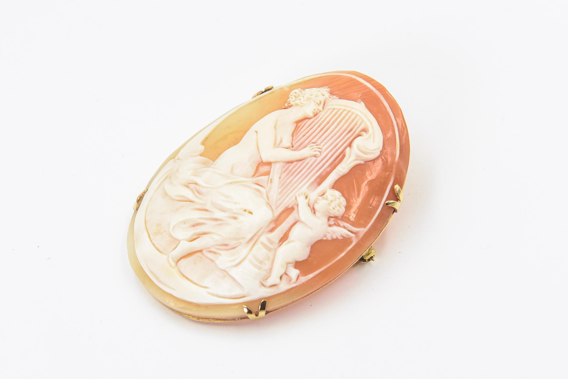 Large 1950s Victorian revival shell cameo featuring a beautiful topless woman playing the harp with cupids assistance.  The cameo is set in an 18k yellow gold from that is marked 750.