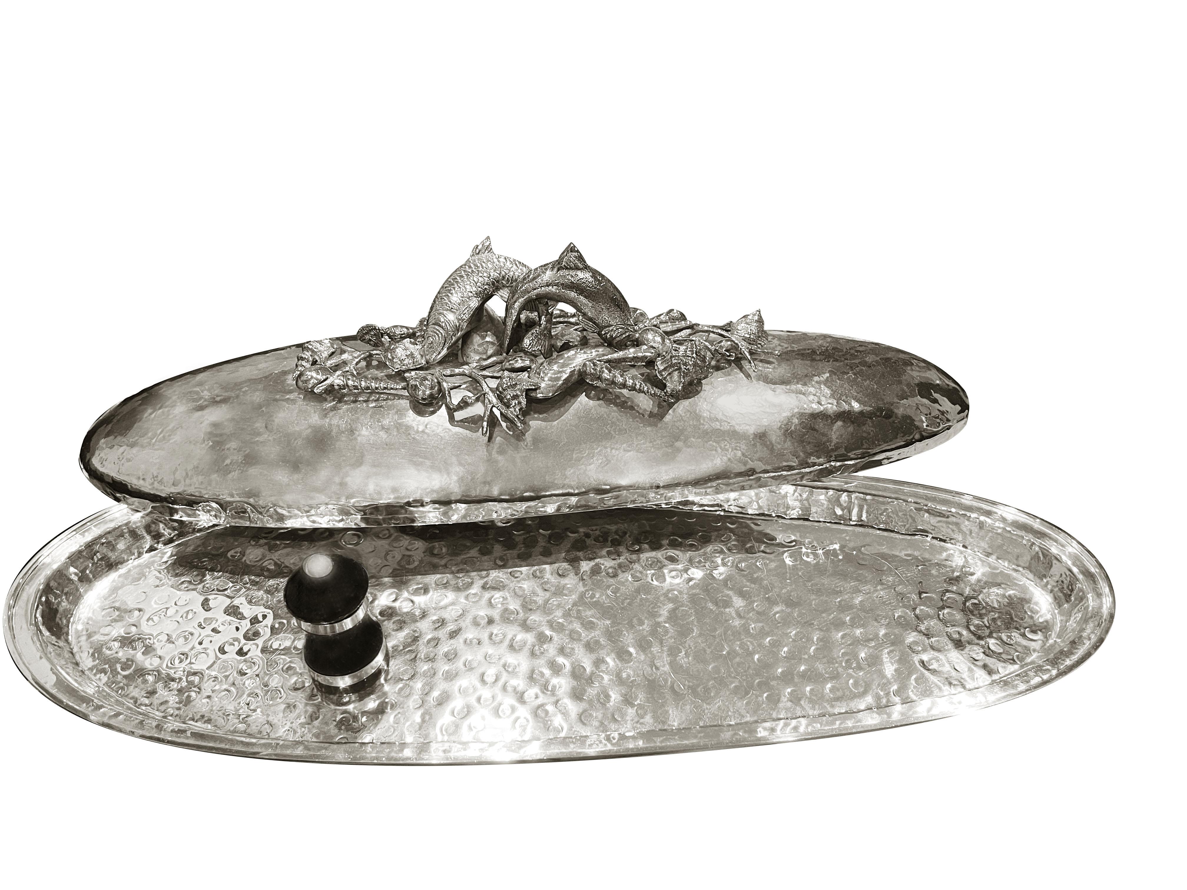 Wunderschöner versilberter, handgehämmerter Fischteller mit Dekorationen aus der Meereswelt: Fische, Seesterne, Seepferdchen und Muscheln zieren den Deckel und werden Ihre Tische verschönern.
Das Franco Lapini zugeschriebene Werk ist auf diese Art