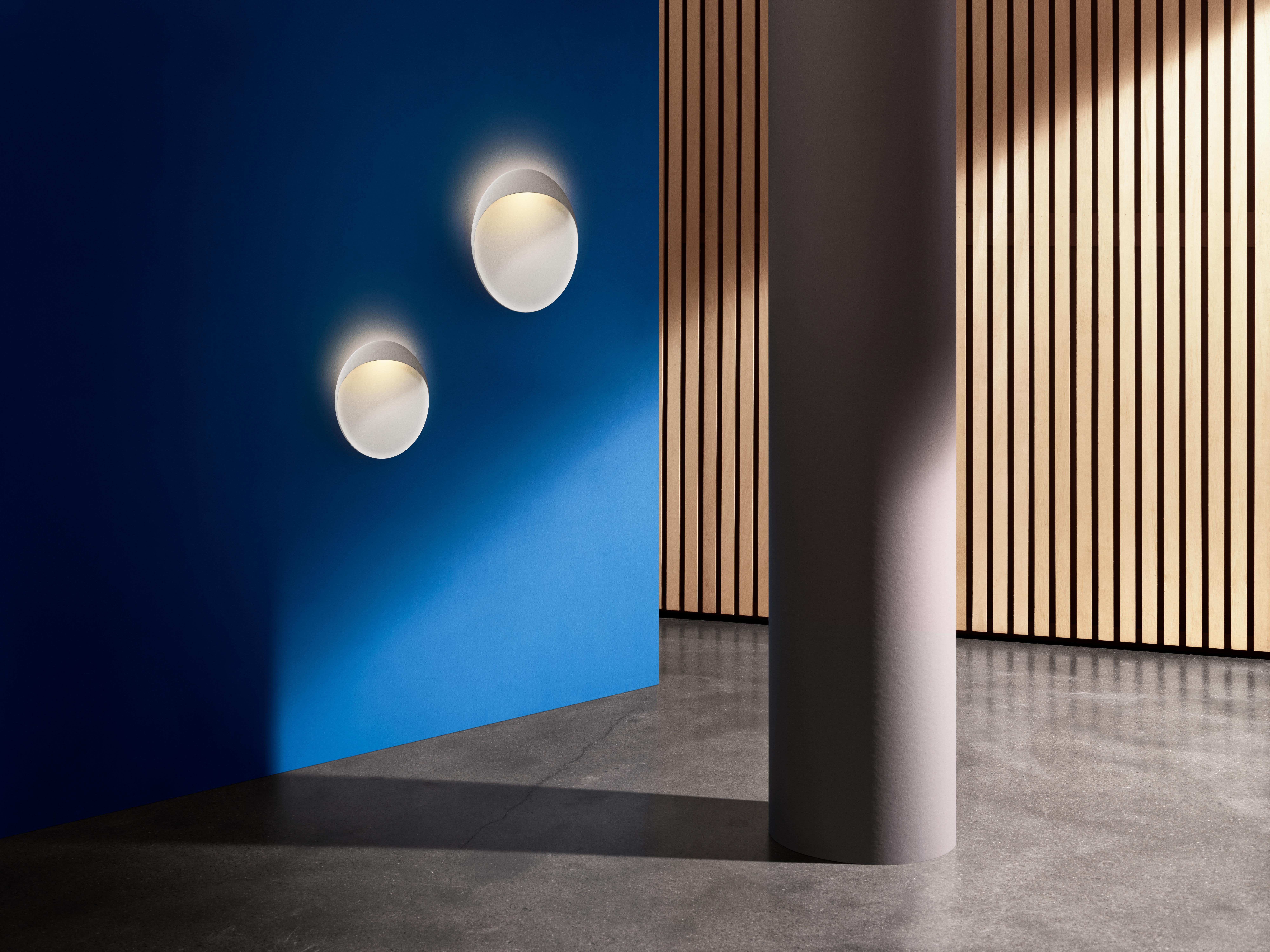 Large 'Flindt' Indoor or Outdoor Wall Light in White for Louis Poulsen.

A circular, wall-mounted fixture that brings bold, sculptural illumination to both indoor and outdoor spaces. The slim, elliptical lamp has a floating appearance that, paired