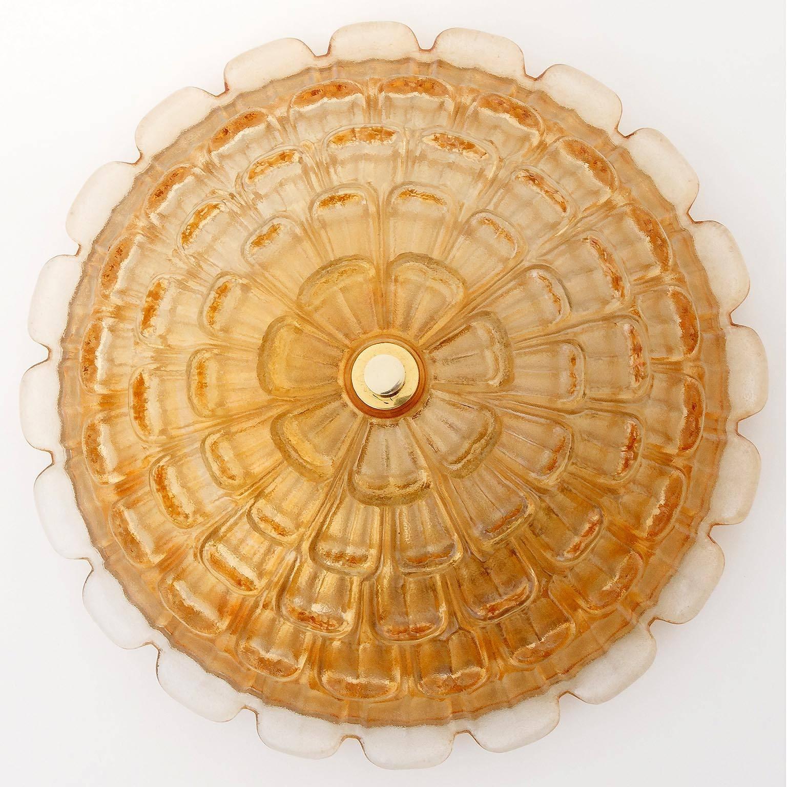 A large and massive floral German ceiling light fixture, manufactured in Mid-Century, circa 1970. 
A textured and amber or orange tone glass is mounted with a brass bolt to an golden painted metal backplate.
The lamp has four sockets for four