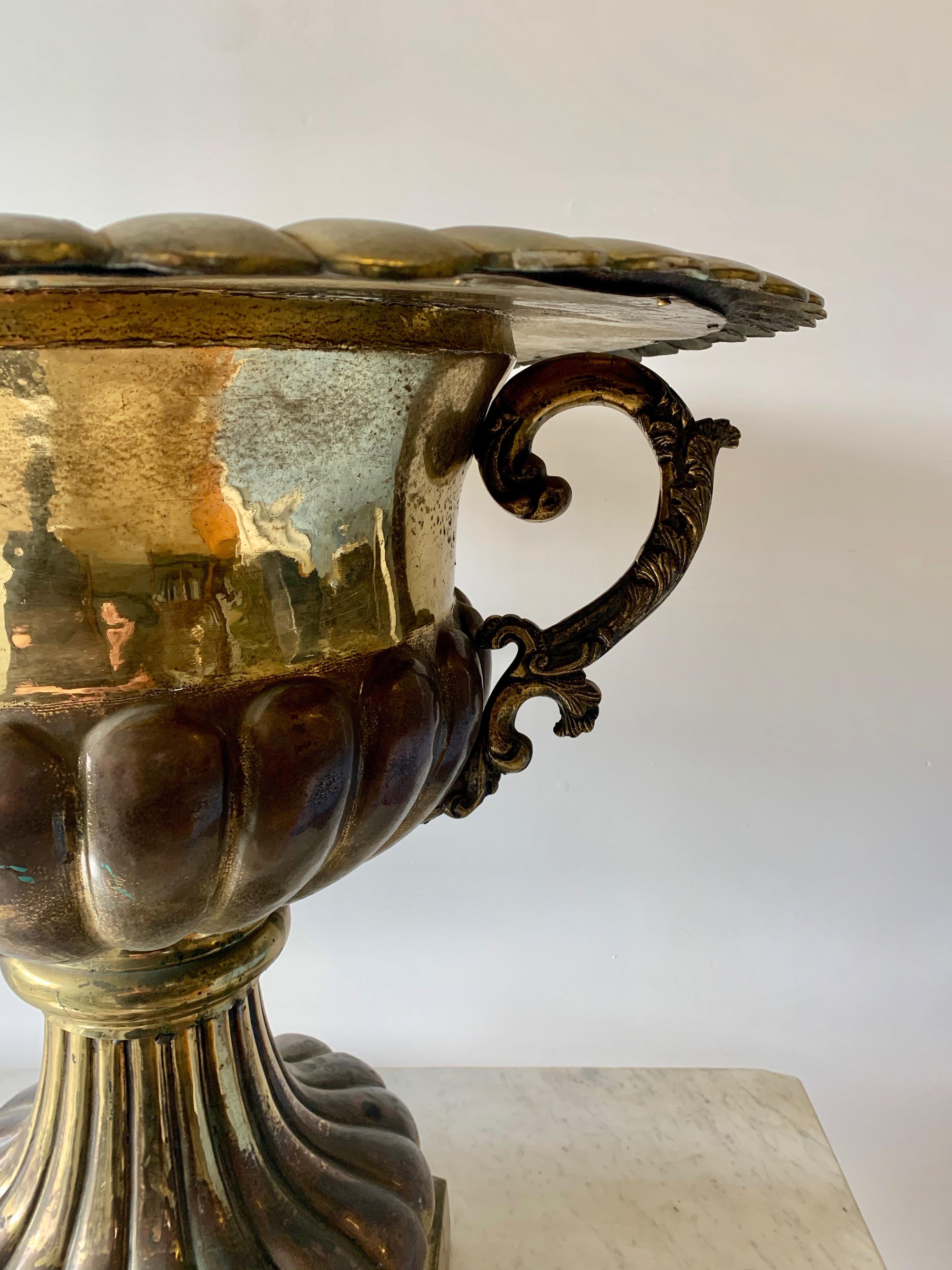 A monumental footed urn in brass with scrolled brass handles. The piece is large enough to house wood, fruit, cuttings or a potted plant - very impressive and inviting
