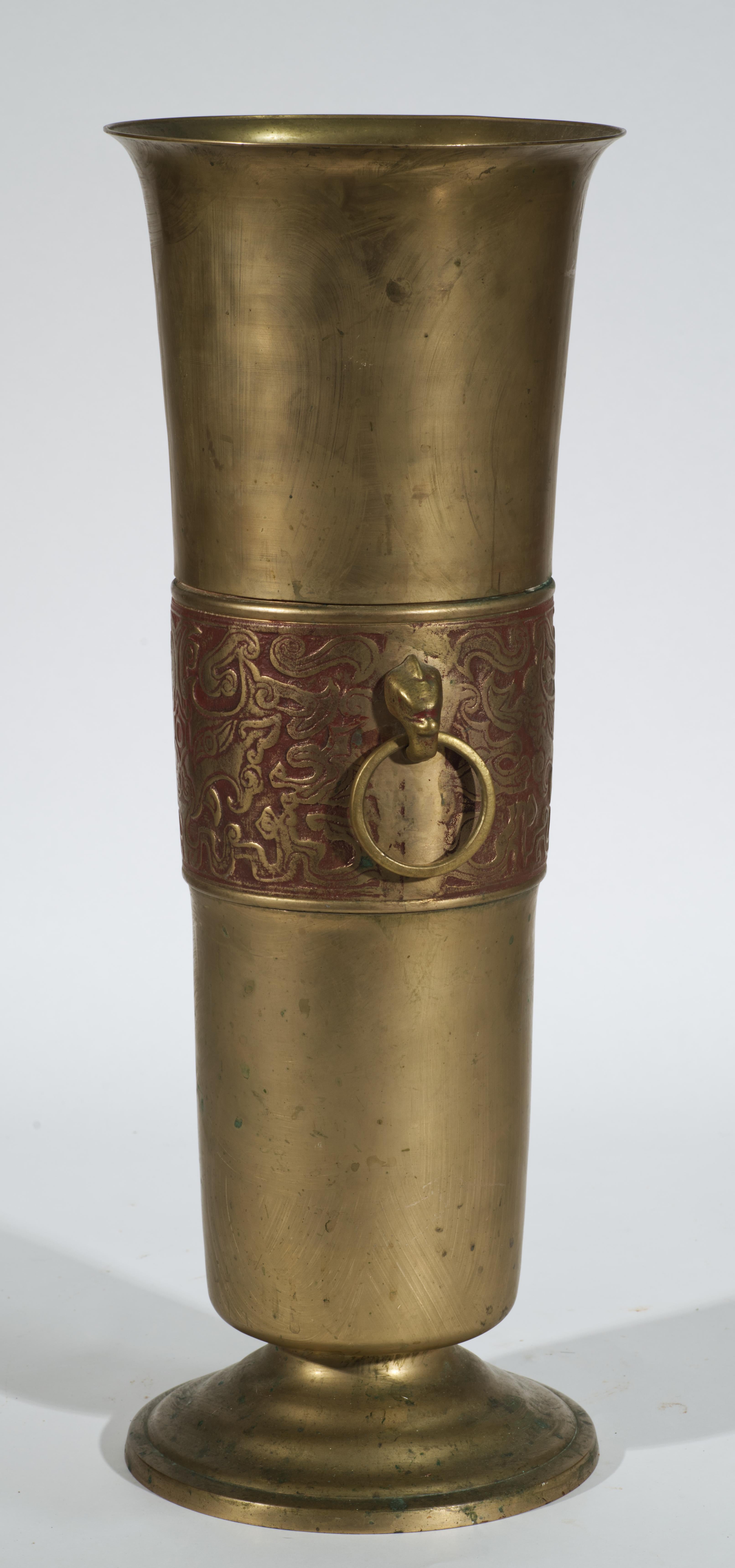 Il portaombrelli o bastone in ottone vintage ha un corpo cilindrico alto montato su un piede rotondo a gradini, decorato con un'ampia fascia di motivi astratti in rilievo e patinati e dotato di due maniglie. La complessa fascia decorativa è