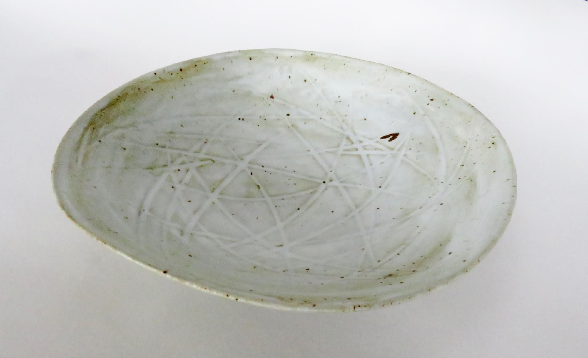Large footed ceramic serving bowl. Glazed in a creamy off-white glaze that allows the color of the clay body to peer through with deep off-white tones and random iron speckling. The interior is lightly carved with geometric lines to give added
