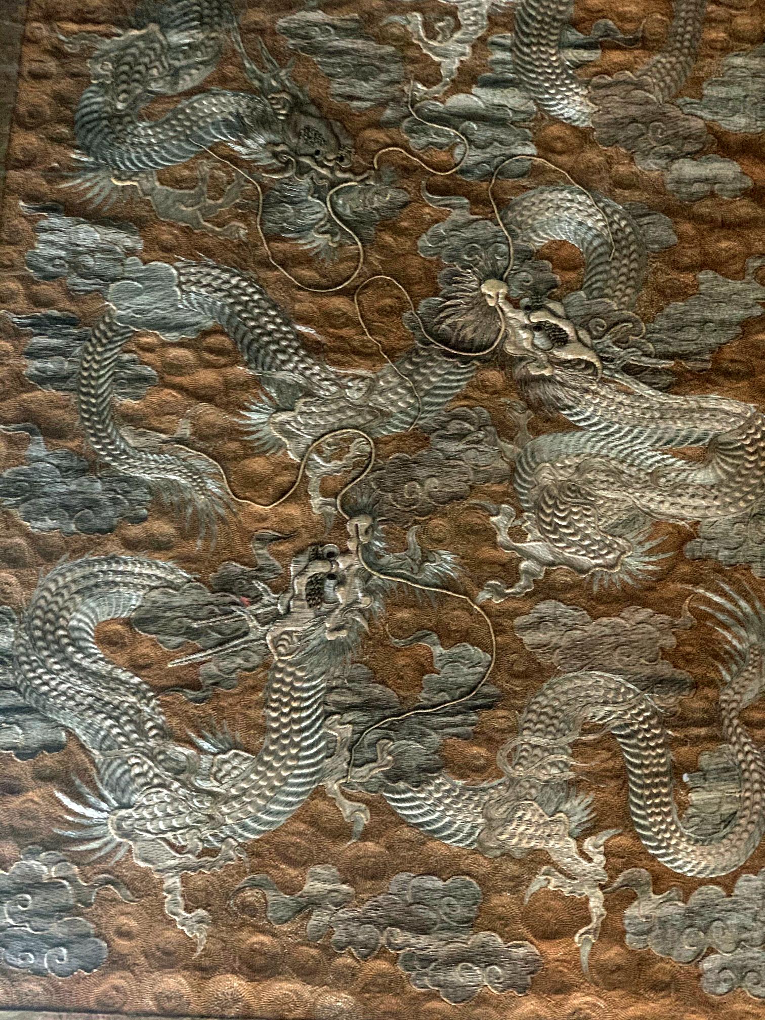 Une impressionnante tapisserie de broderie japonaise vers 1890, période Meiji, présentée avec une bordure de brocart sur toile de lin dans une boîte à ombre en Lucite. Le design époustouflant représente trois dragons qui s'enroulent et volent dans
