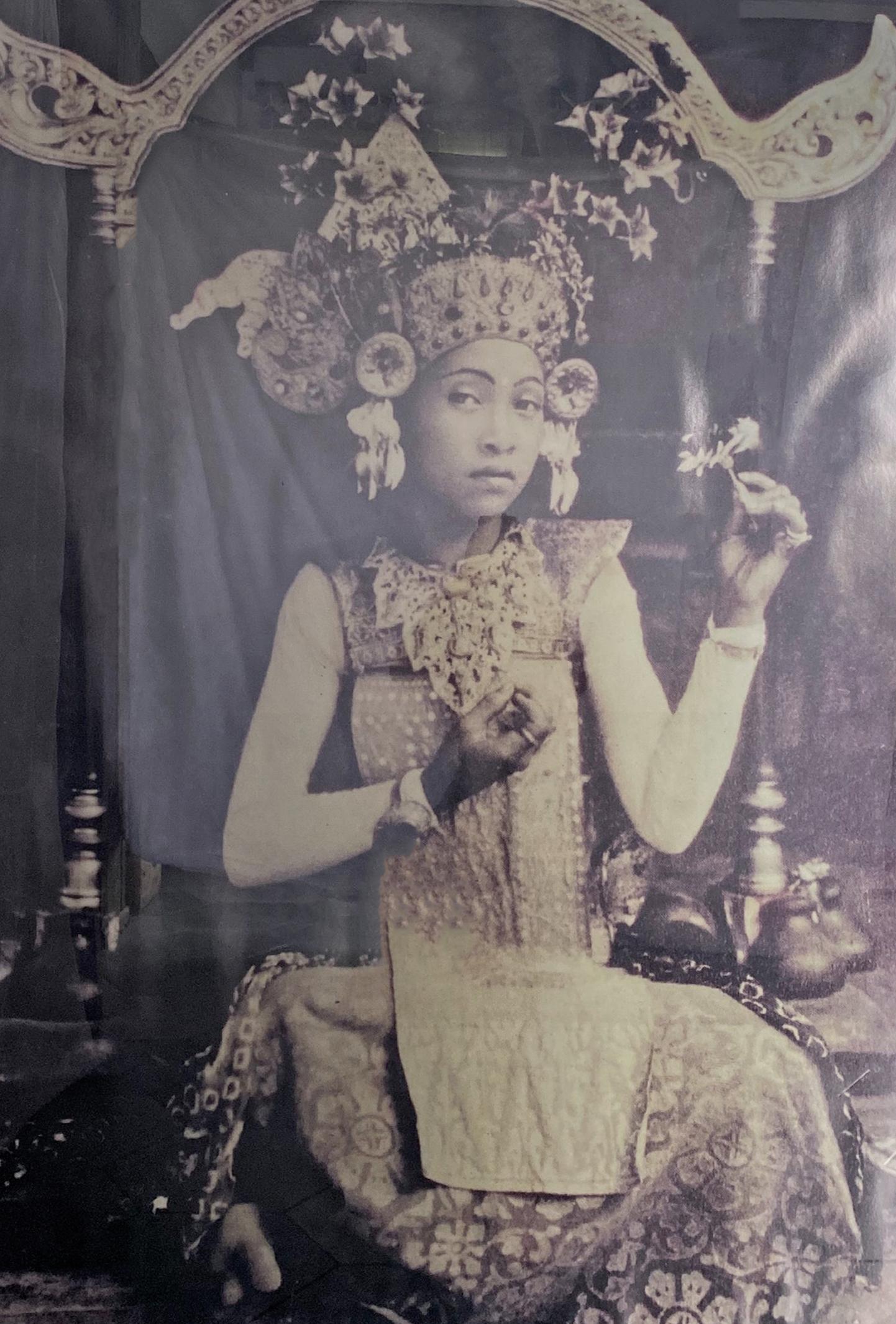 A relatively large photograph from Bali, Indonesia framed in a wood & glass frame. The black & white photo captures a young balinese girl in traditional ceremonial attire. 

Measures: height 163 cm x width 115 cm x depth 2 cm. 

