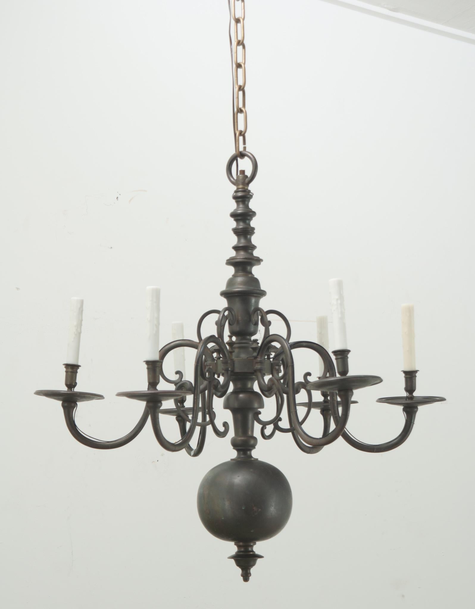 A large antique six light heavily patinated brass chandelier. The center of this fixture is turned and shaped and ends with a substantial ball finial. There are six curving arms with tall faux candle covers. This chandelier has been cleaned and