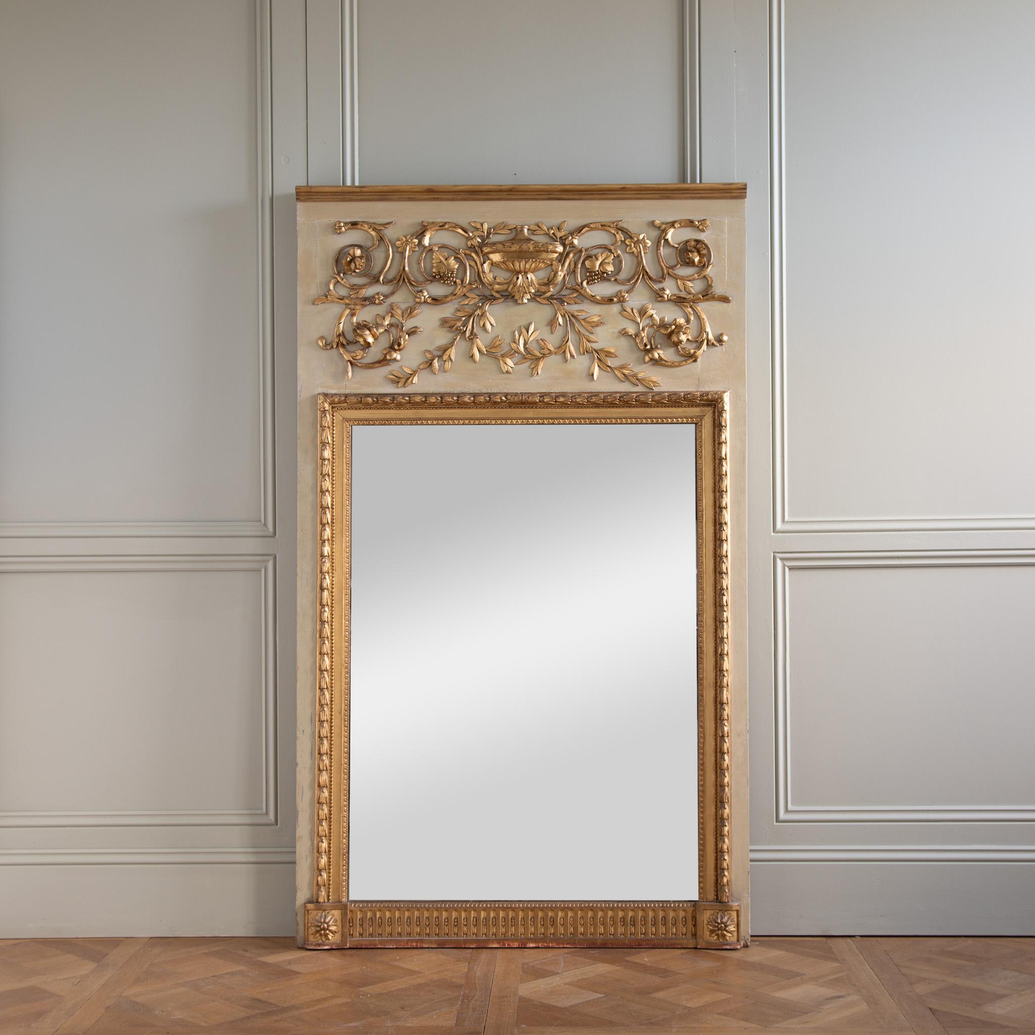 Questo grande specchio trumeau in stile Luigi XVI, proveniente dalla Francia verso la fine del 1800, ha proporzioni generose che lo rendono una presenza imponente. 
Il raffinato intaglio decorativo, nella parte superiore del Trumeau, presenta