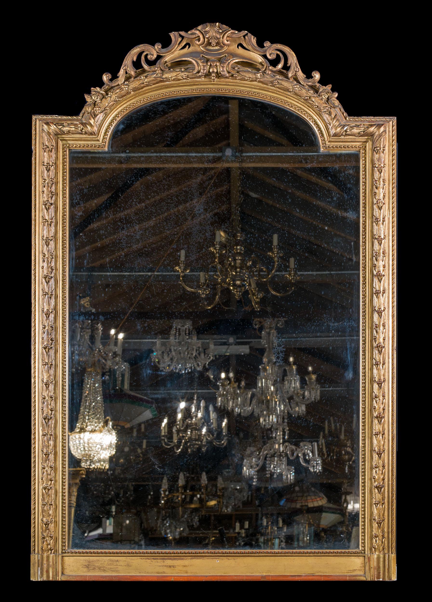 Grande specchio francese in gesso dorato con frontone ad arco a volute. La cornice è decorata con alloro legato e modanature a corda, bordate da una raffinata perlinatura. Sul verso è presente un frammento di etichetta del produttore che data lo