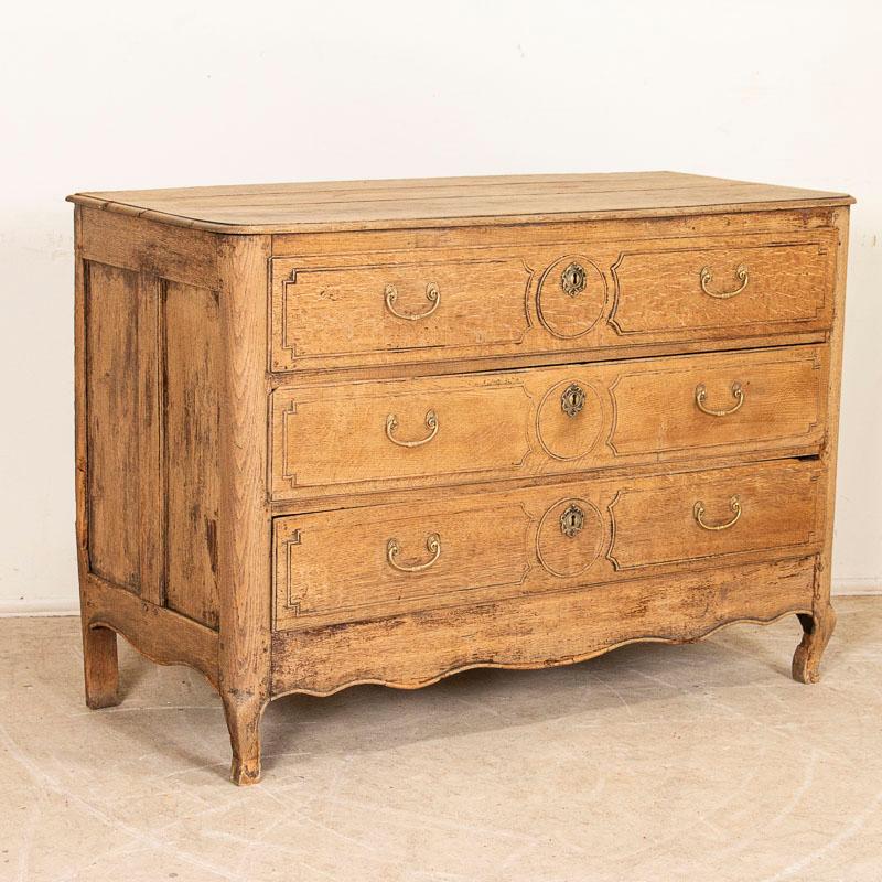 This classic French oak chest of drawers has been given new life with a bleached finish which lightened the dark oak and brings out the lovely carved details of the paneled drawers and sides. Double brass pulls accent the 3 large drawers, original