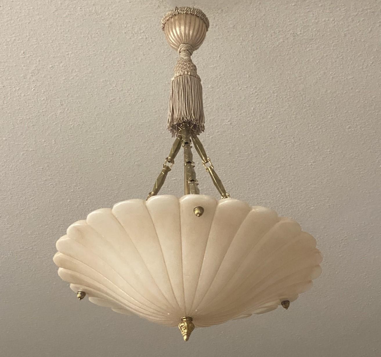 A wonderful Arte Deco three-light fixture chandelier from the 1920s manufactured in France. Large hand-carved  and polished white alabaster shade suspended by three brass chains connecting to original handmade silk tassel fringe rope and tassel