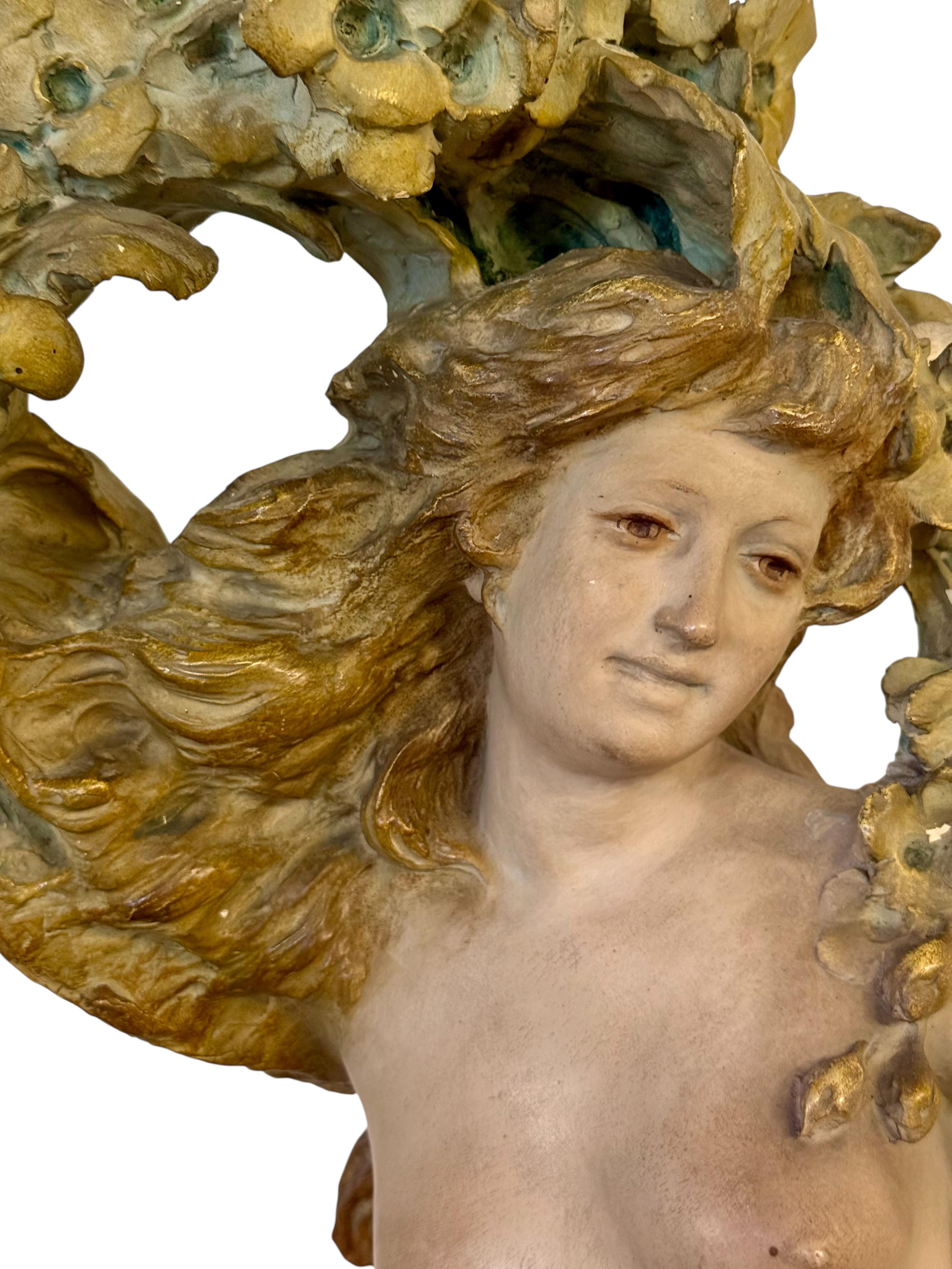 This stunning Art Nouveau sculpture is a large-scale painted plaster figure of a partially draped female nude adorned with flowers and flowing drapery. Sculpted with remarkable grace and movement, the figure captures the essence of nature-inspired