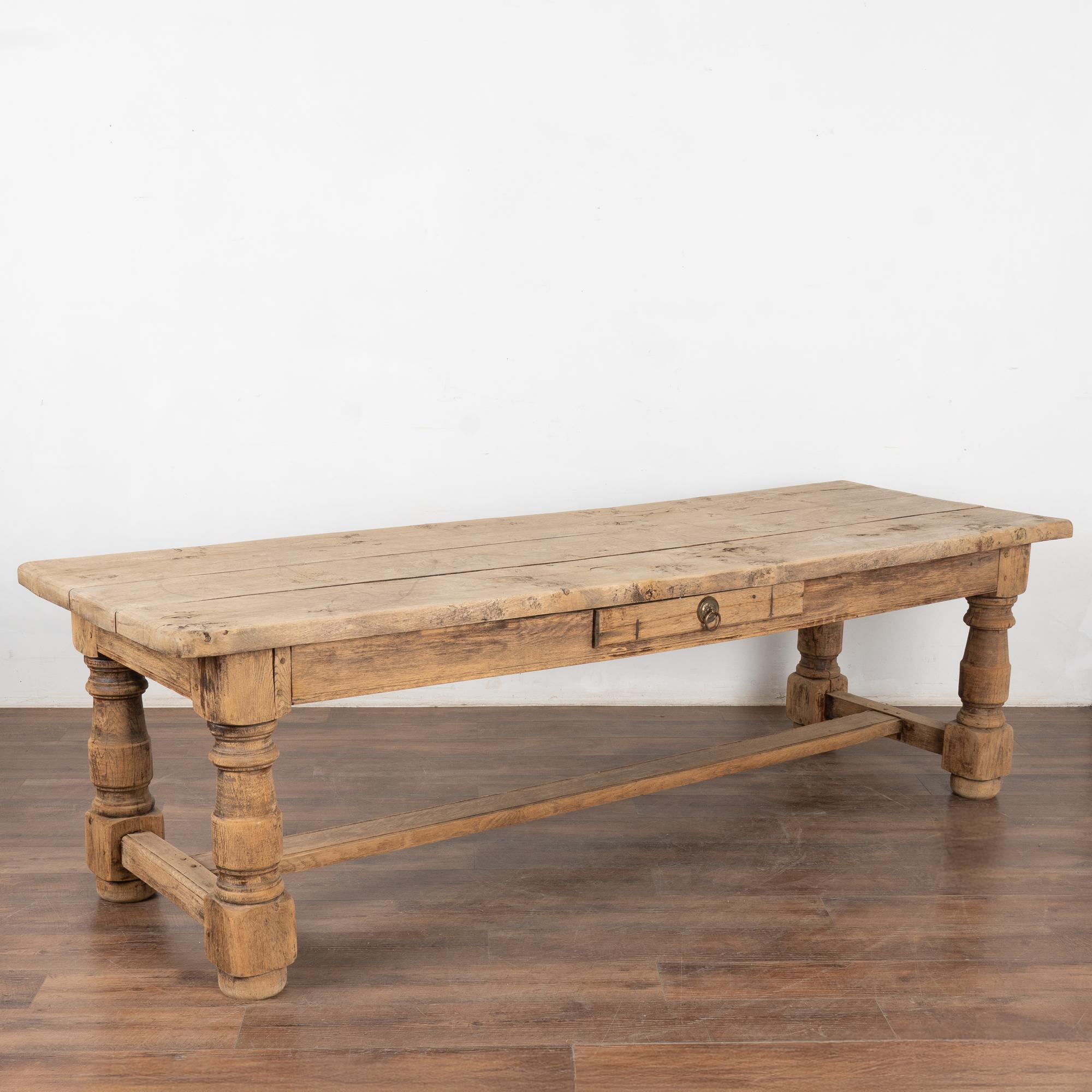 The aged patina of the bleached oak wood draws one to this handsome refectory or library table from France.
The heavy turned legs of the trestle base add to the visual appeal.
Note in close up photos the wood grain, old nicks, cracks, stains and