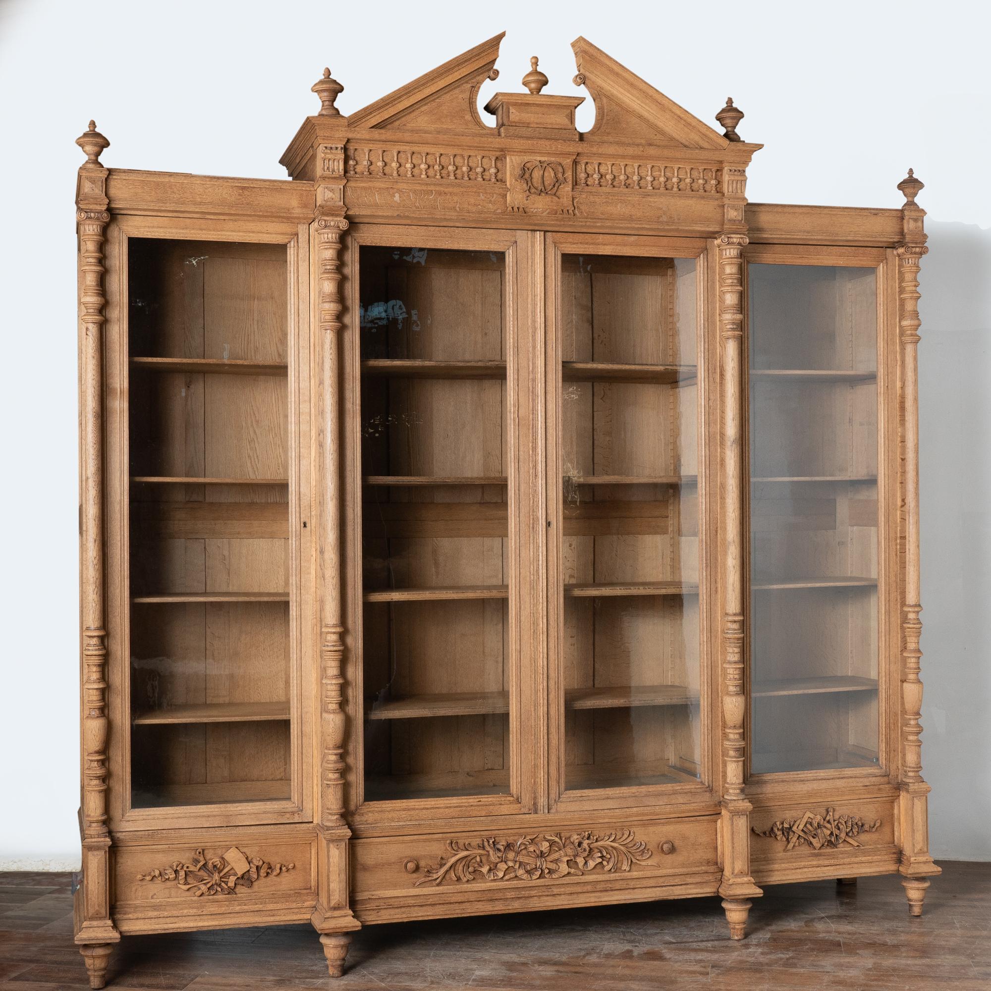 Questa imponente libreria o vetrina in rovere sbiancato è dotata di quattro lunghi pannelli in vetro e supera di poco i 10' di altezza e larghezza.
Nota le colonne tornite, la corona scenografica e gli intagli decorativi lungo i tre cassetti.