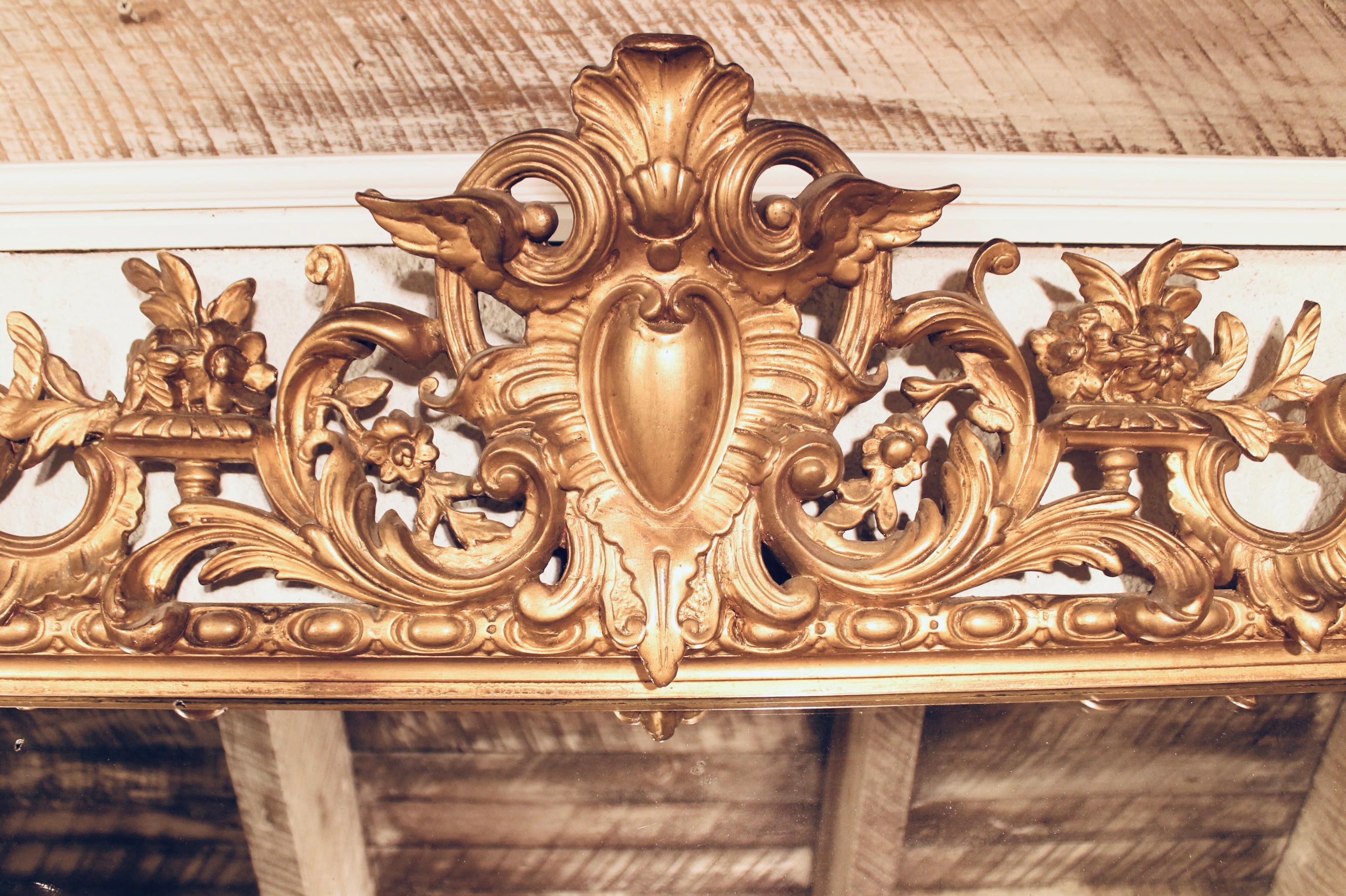 A large and impressive gilded pier mirror, the crest with a winged cartouche set among exuberant Rococo scrolling forms at the center. Pearl borders, a variation on egg and dart moldings and elongated cartouche corners complete the surround. The