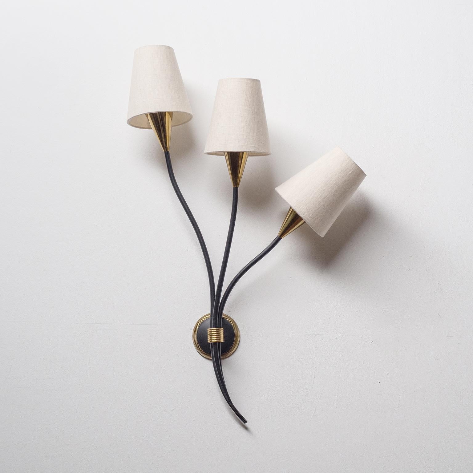 Rare French wall light from the 1950s, attributed to Arlus. Three organically curved arms with original black lacquer. Brass and ceramic E14 sockets with new wiring and linen shades.