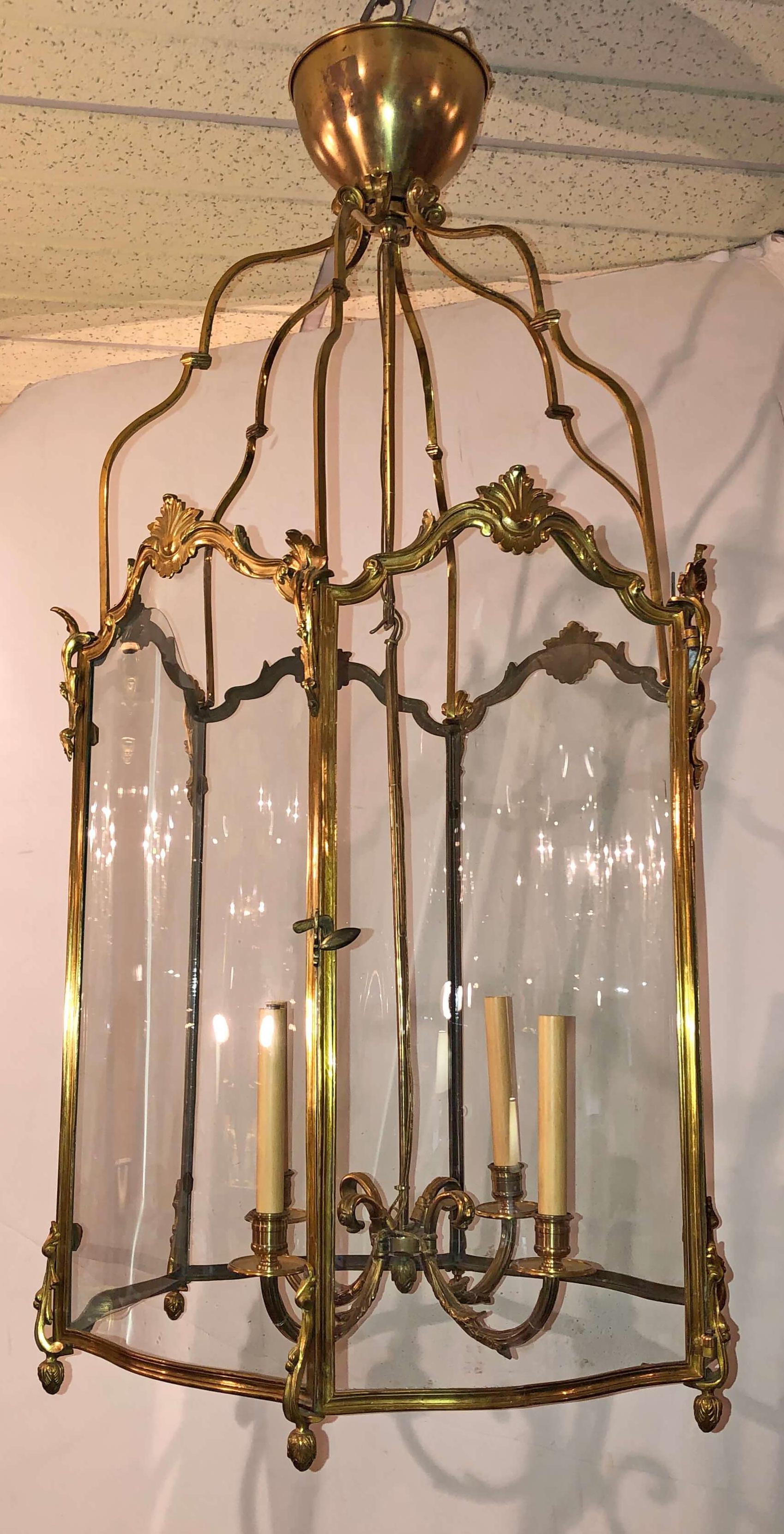 A fine and large French gilt bronze hall lantern with serpentine glass sides, working door, four-light hanging cluster, acanthus leaf decor, and acorn finials.