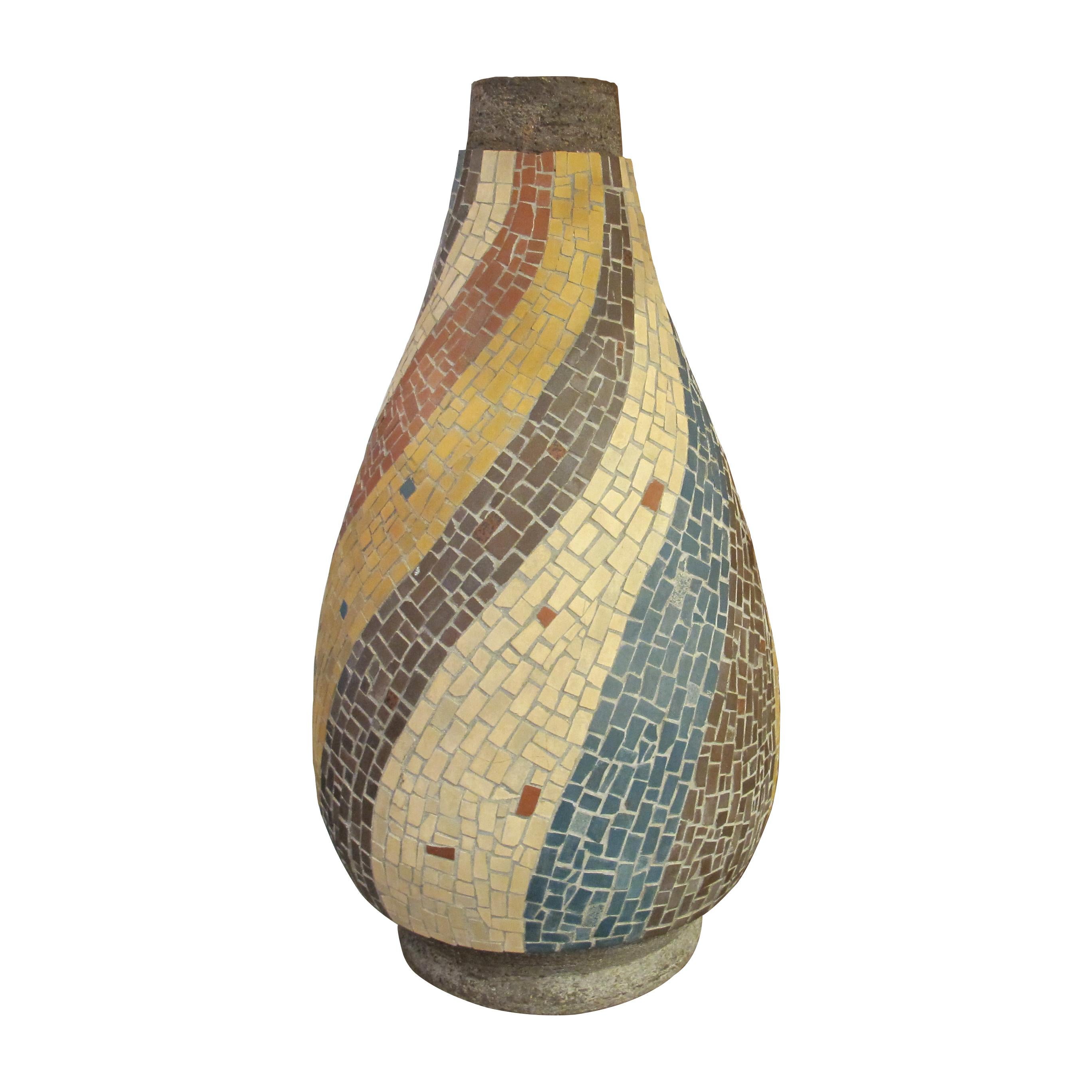 This is a very large French ceramic vase from the 1950s. it features an elegant, elongated teardrop shape and is richly adorned with a colourful mosaic tile design. Flowing bands of yellow, terracotta, cream, grey, blue, and beige tiles spiral