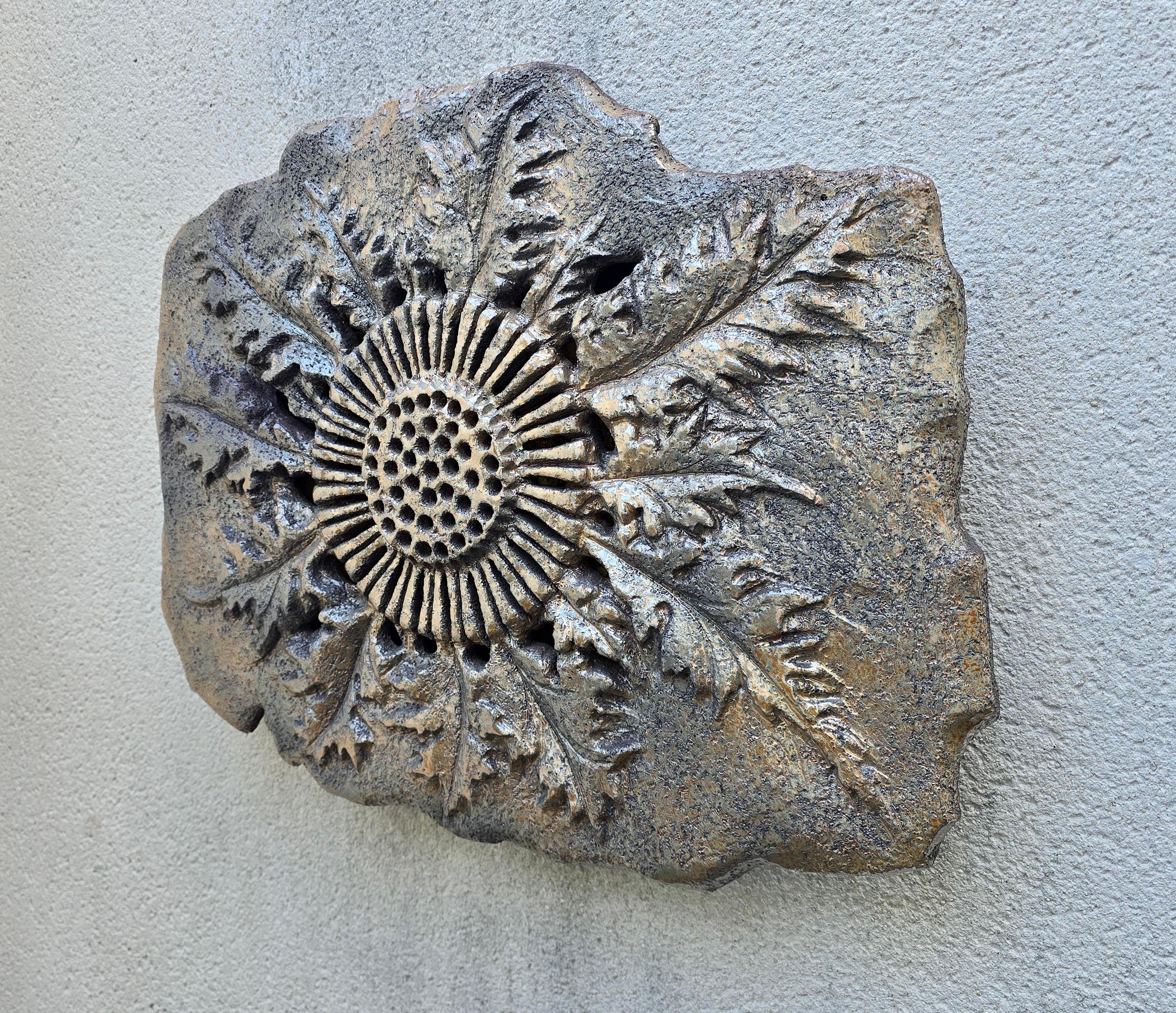 Grande sculpture lumineuse en céramique, signée et réalisée en France dans les années 1970. Le motif de soleil sculpté à la main et la surface texturée en chamotte rappellent les traditions de l'Art Brut et de Vallauris. Une chaude lumière ambrée