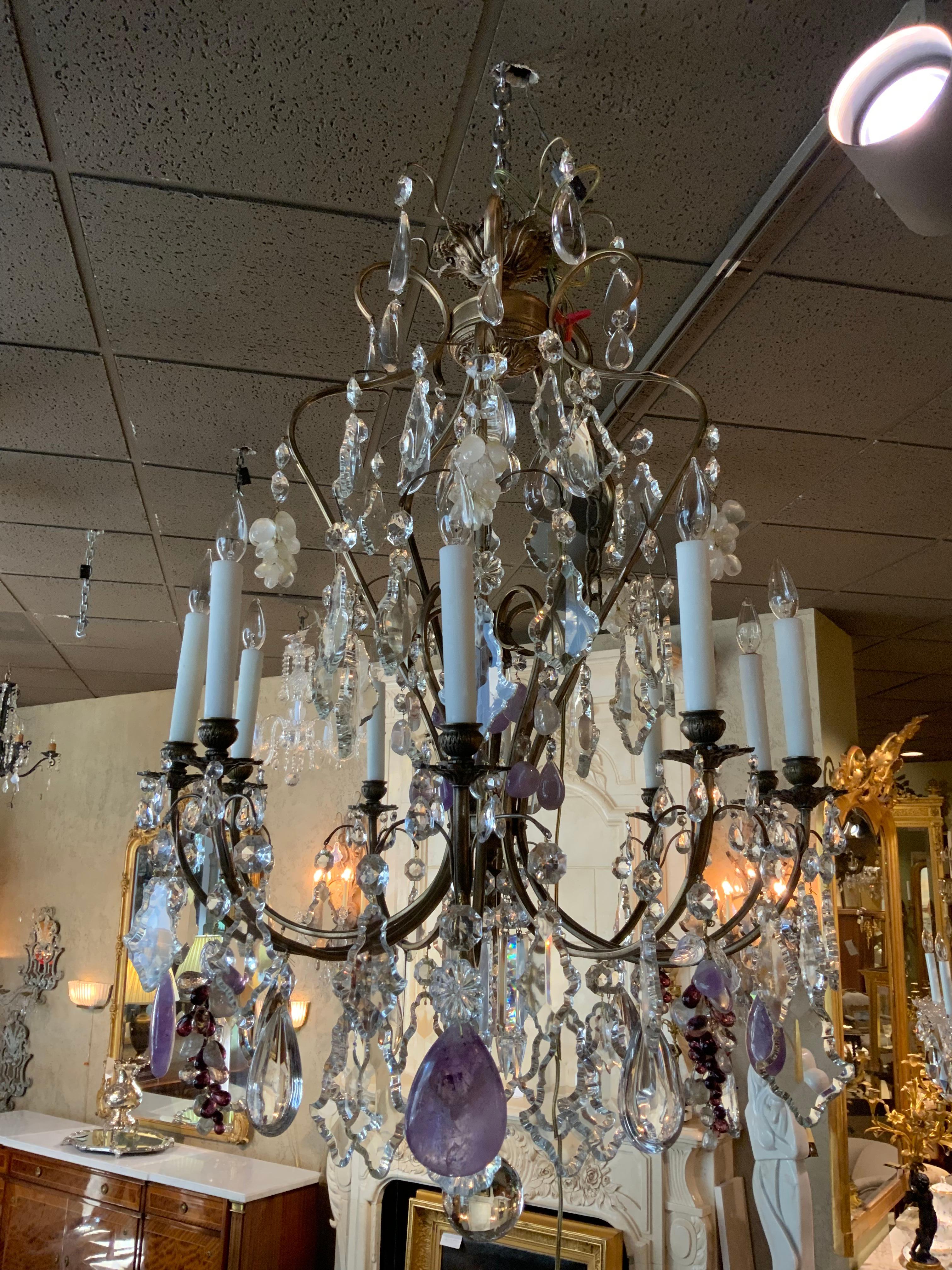 Large crystal chandelier with ten lights around the perimeter and having antique bronze
Scrolling arms. Grape -like clusters of crystal in amethyst and rock crystal are scattered
Throughout this fixture. Large scrolling arms adorned with amythest