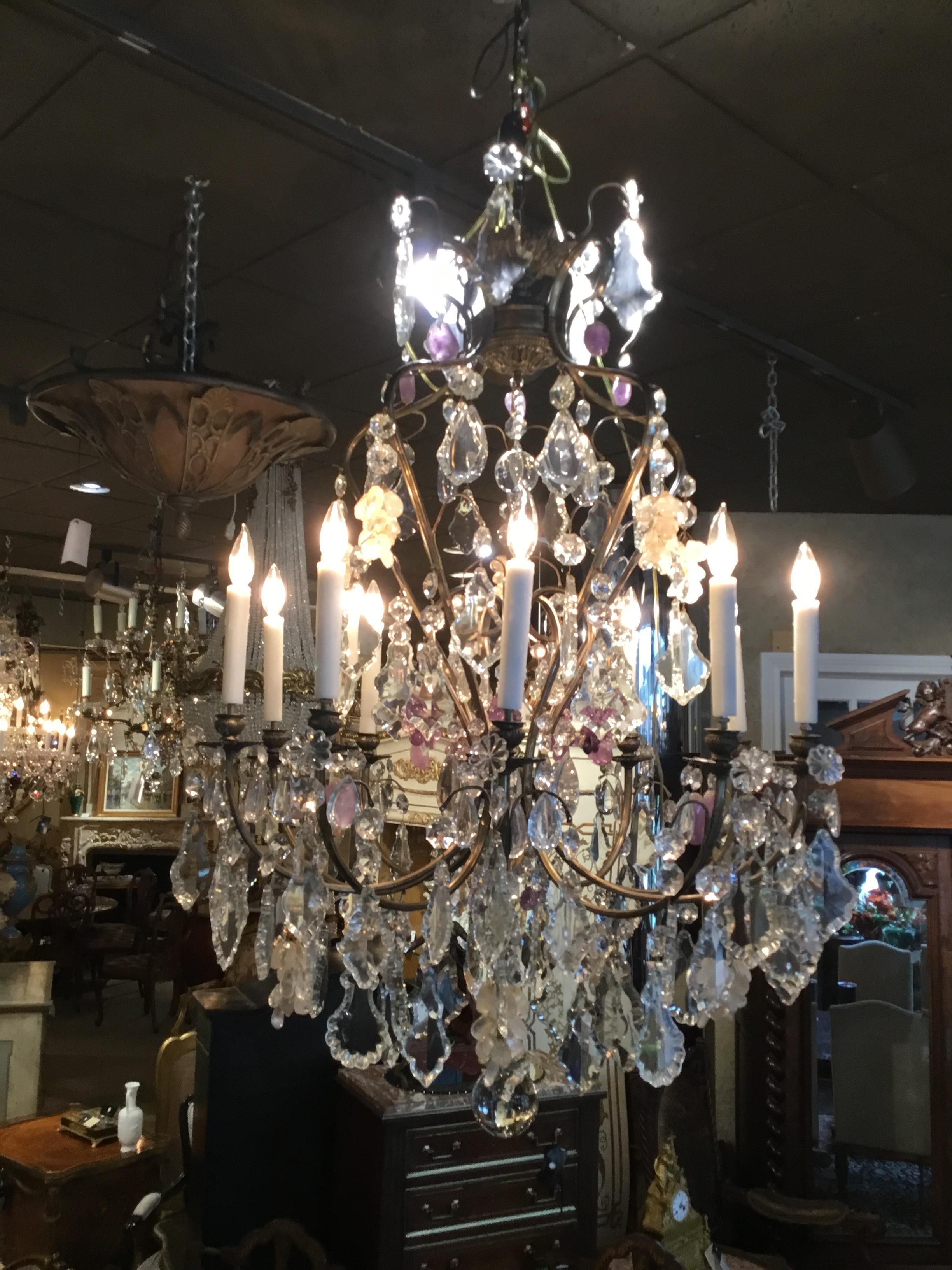 Large crystal chandelier with ten lights around the perimeter and having antique bronze
Scrolling arms. Grape -like clusters of crystal in amethyst and rock crystal are scattered
Throughout this fixture.