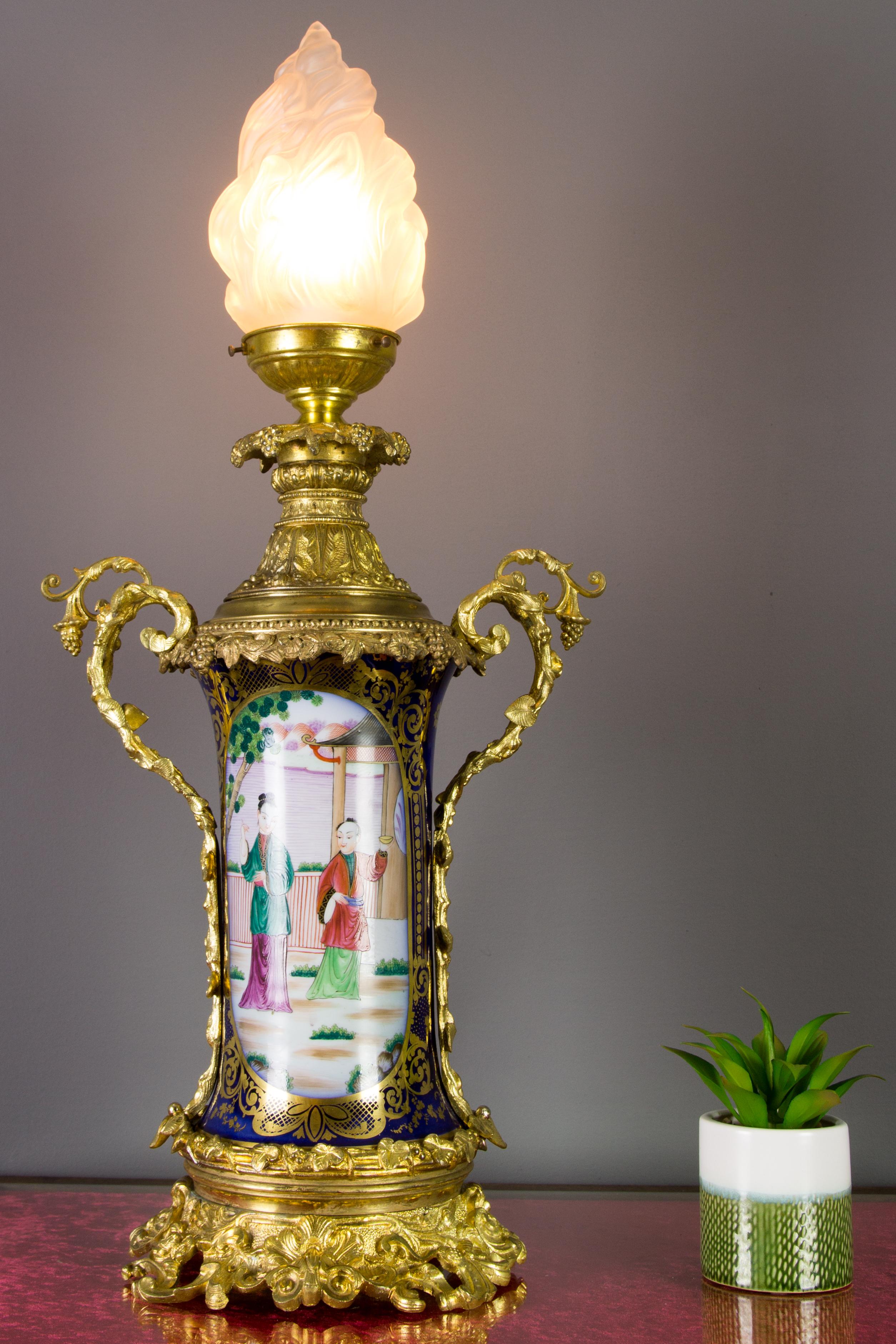 This amazing and large late 19th-century oil lamp mounted on a gilt bronze base and fitted with bronze cap and handles, features a cobalt blue and hand-painted porcelain body with chinoiserie style colorful scenes. Ornate gilt bronze details in
