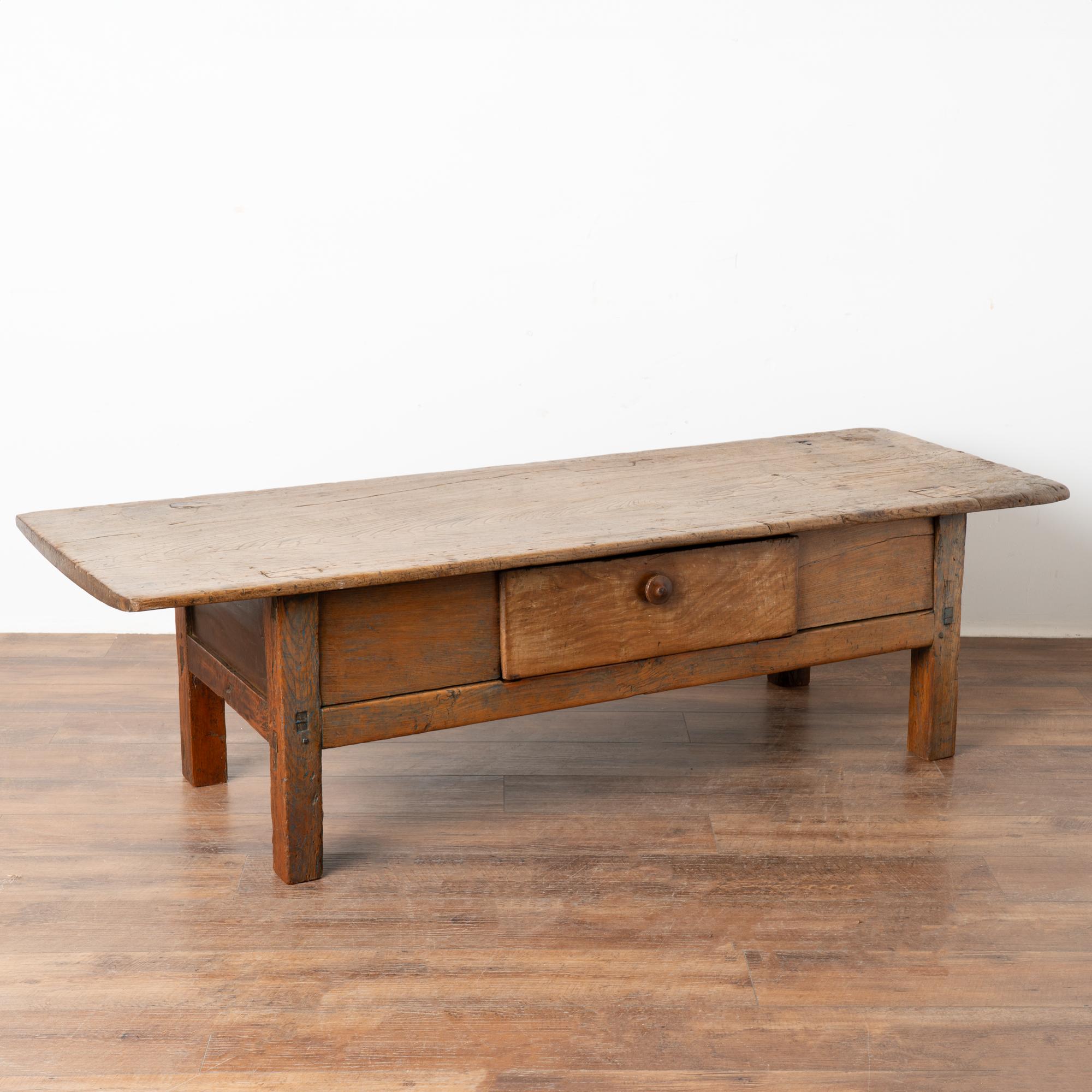 The beauty of this French country coffee table with one large drawer comes from the warm aged patina of the wood. Every crack, ding, old knot and stain all add to the depth and richness found in the worn top. There is faint residual blue paint that