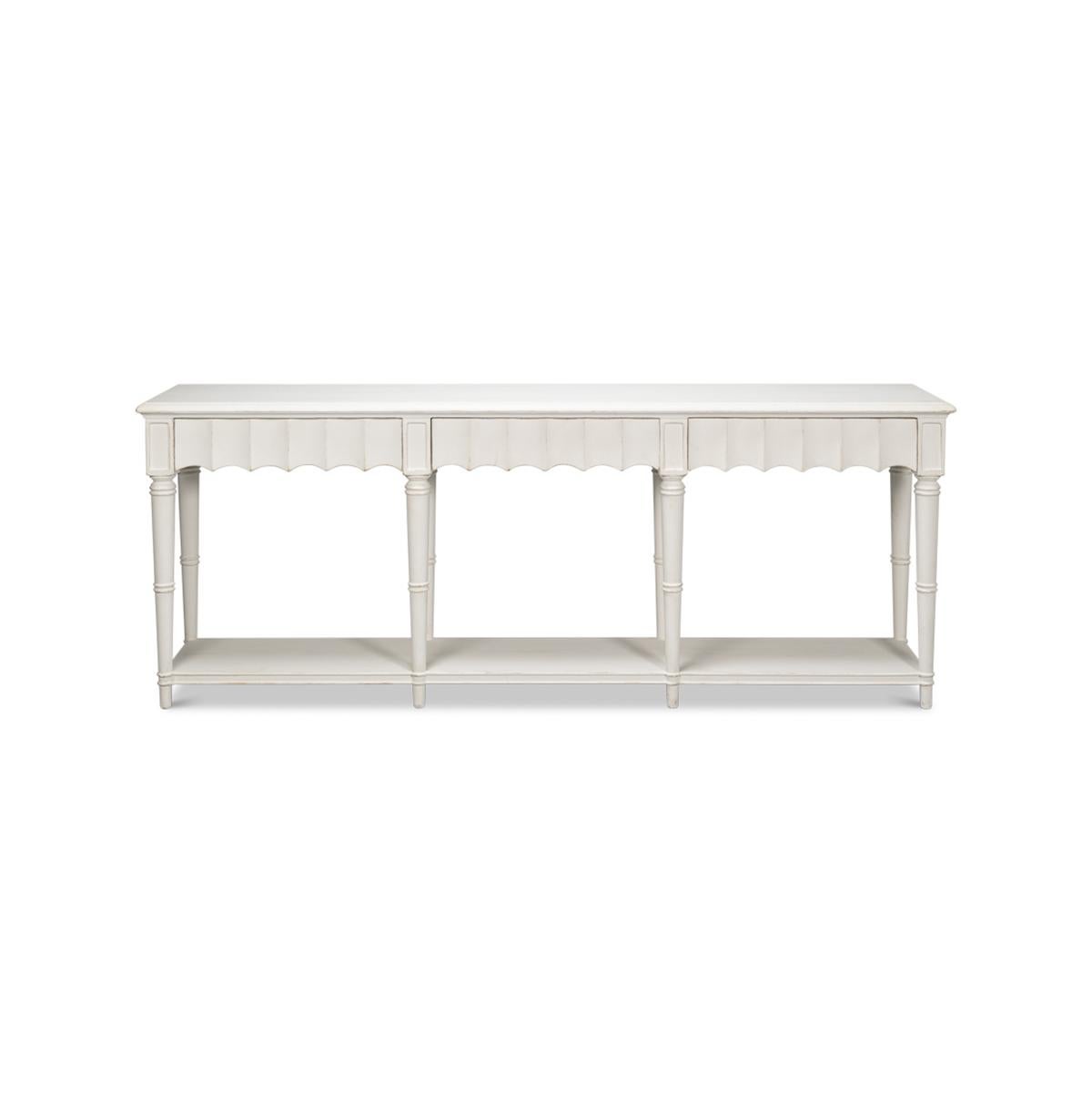 A Country console table in a hand-rubbed antique white finish. The front apron of this piece has a beautiful fluted design. It has three drawers, eight turned and tapered legs, and a shelf stretcher base. 

Dimensions: 93