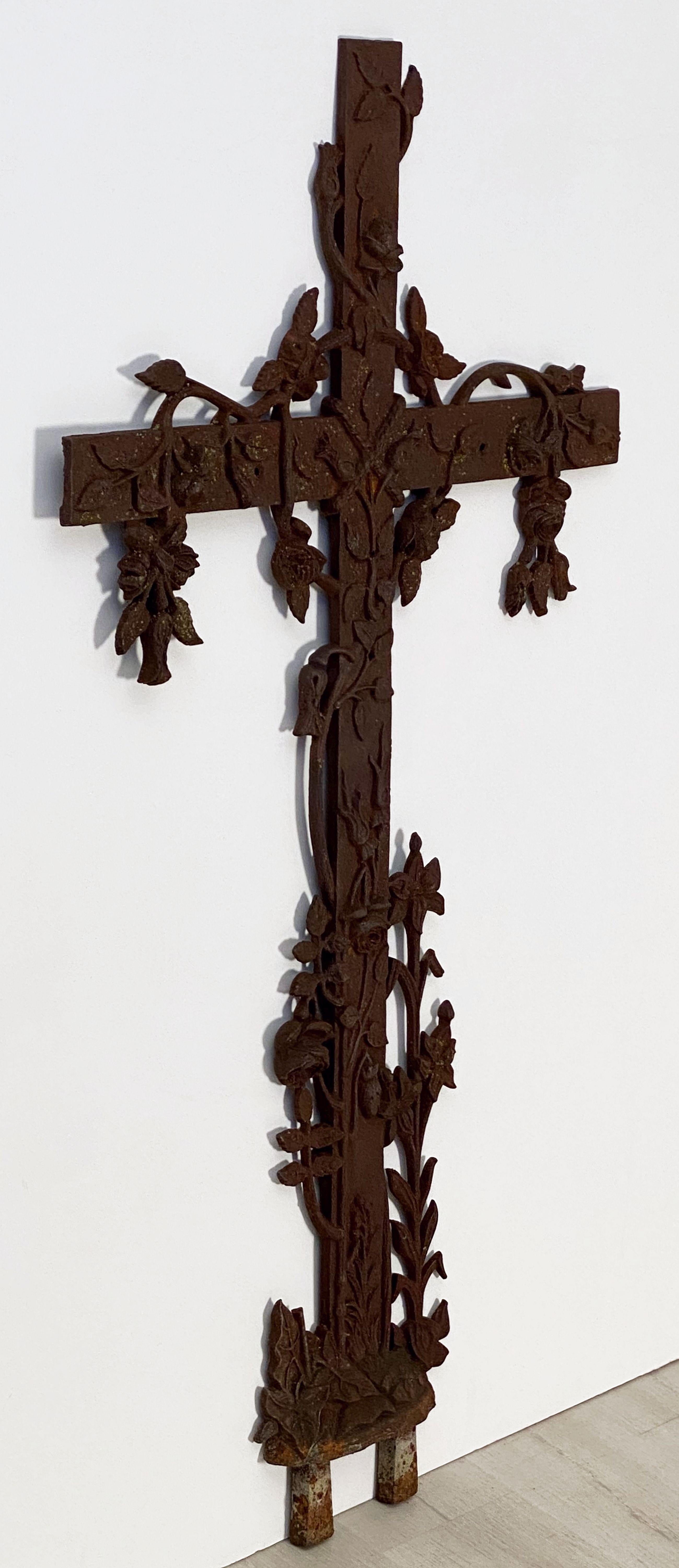 A large French cross of cast iron with featuring a decorative foliate design with roses and ivy on the top, arms, and base.

Dimensions are 
H 50 1/2 inches
W 27 inches
D 1 3/4 inches.