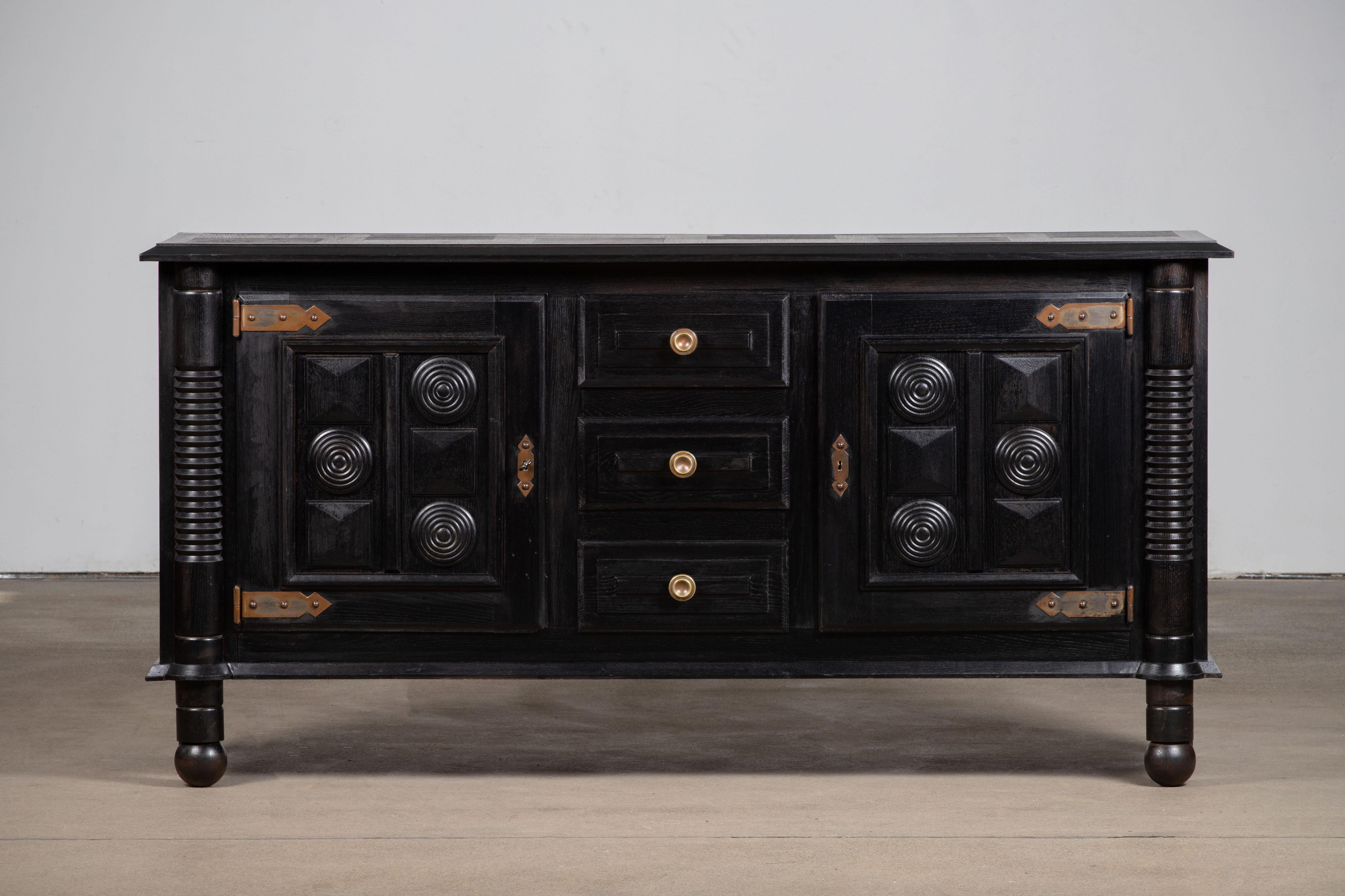 A large sideboard/credenza in solid ebonized oak attributed to Charles Dudouyt, France, c1940s.
Consists of 3 central drawers and two storage compartments. 
Original brass detailing and graphic design doors make this piece really stand out.
The