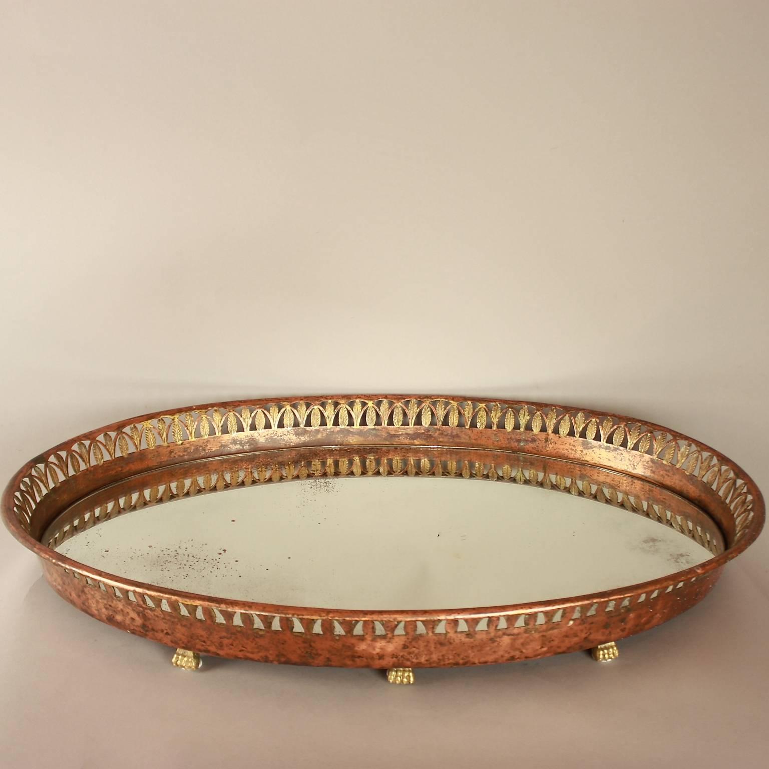 An Empire mirrored oval centerpiece, a so called 'surtout de table', with its original mirror surrounded by a pierced and chased gallery depicting a leave frieze. The copper centerpiece with remnants of former gilding raised on gilt-bronze lion paw