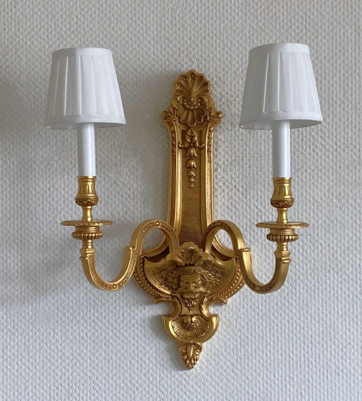A precious gilt bronze two-light wall sconce in the Louis XV style, France, 1920-1929. Finely elaborate with hand chiseled details. Typical design of French Empire period due to its rich ornamentation with faces and acanthus leaf motifs. The bottom