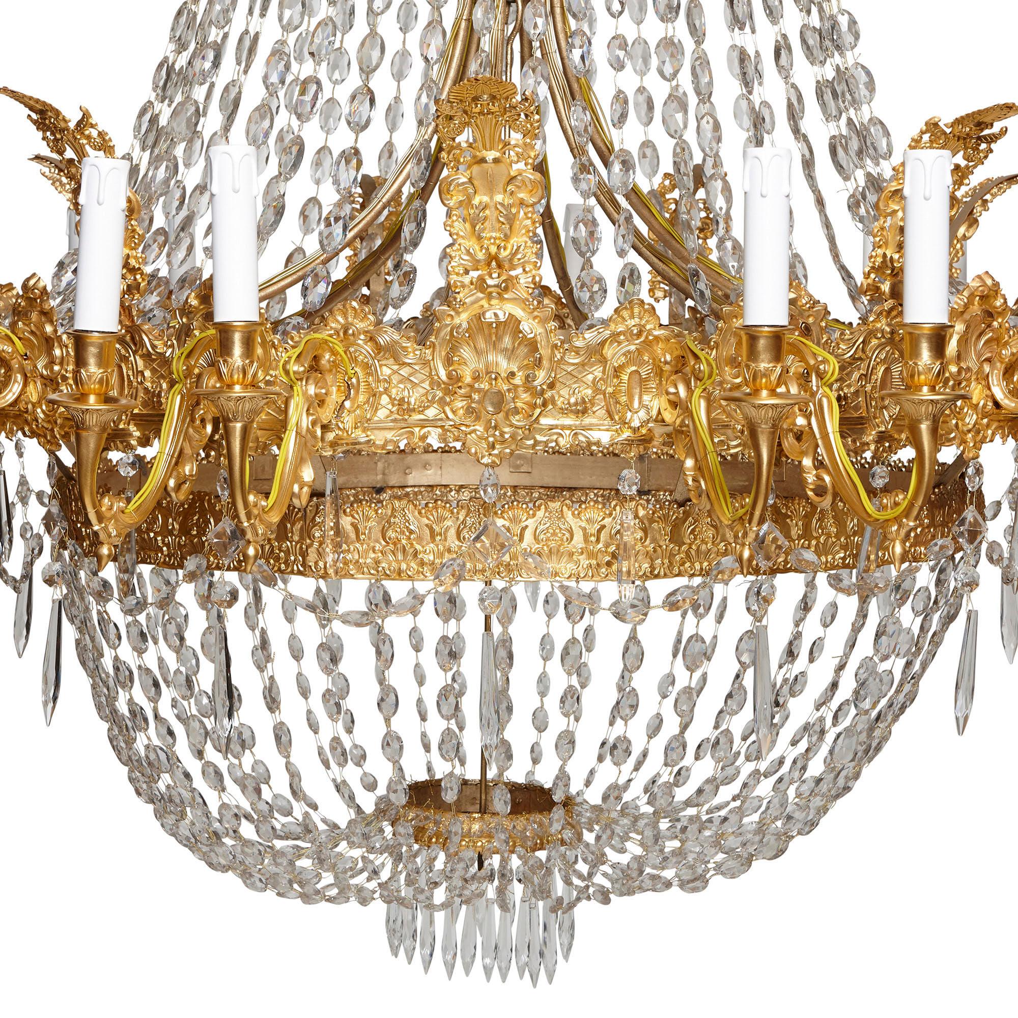 This 19th century French chandelier is designed in the Empire style and wrought from gilt bronze and strings of cut glass. The chandelier features a lower dome-shaped body below an overarching tent-shaped canopy. The top of this canopy, which is