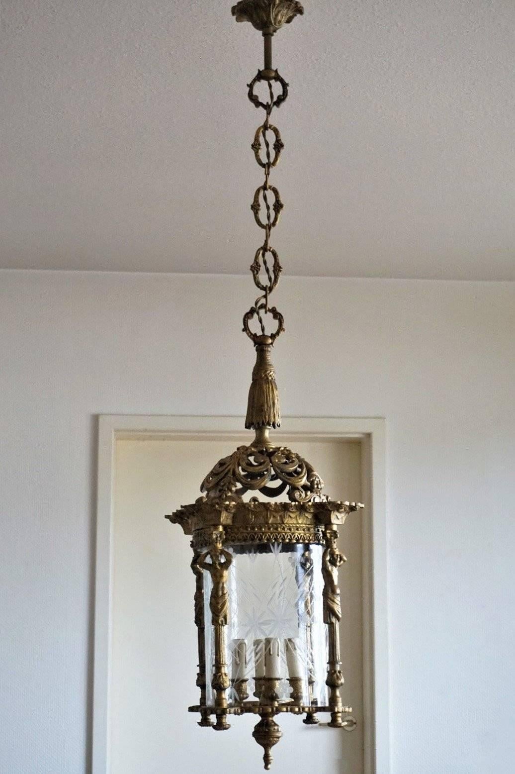 A large late 19th century Empire style four-light lantern of gilt solid bronze with cut-glass cylinder. Heavy bronze richly elaborate with four figurine columns, beautiful solid bronze chain and canopy.
The lantern is in very good condition with