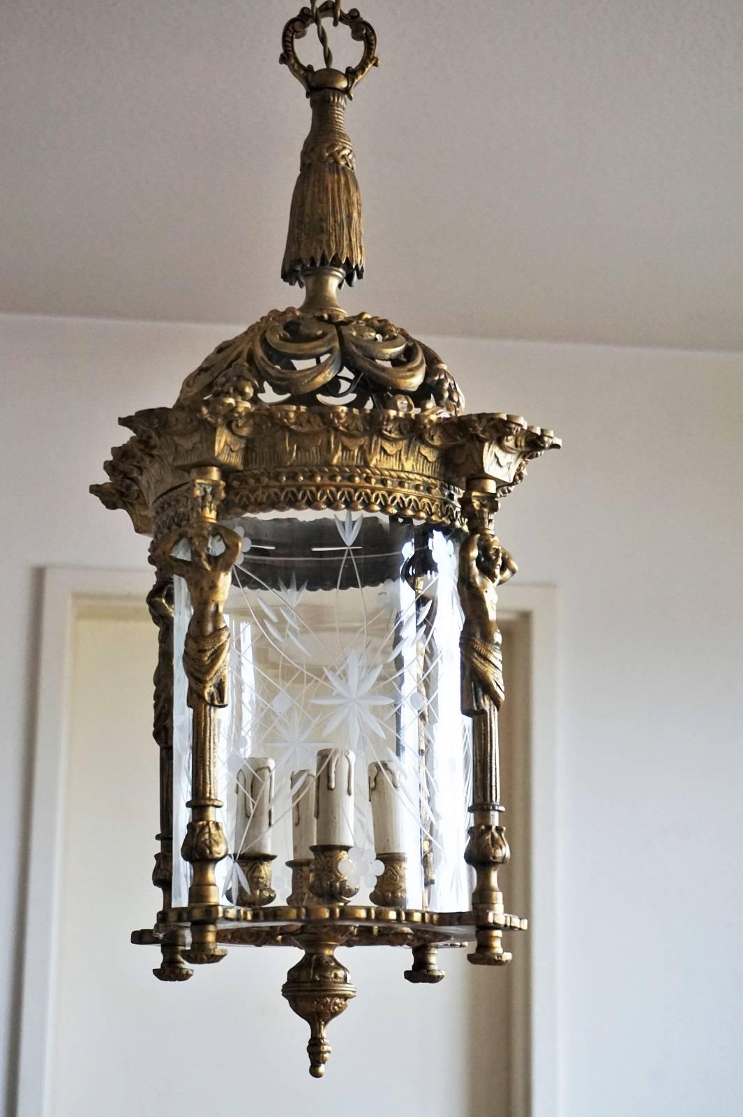 A large late 19th century Empire style four-light lantern of gilt solid bronze with cut-glass cylinder. Heavy bronze richly elaborate with four figurine columns, beautiful solid bronze chain and canopy.
The lantern is in very good condition with