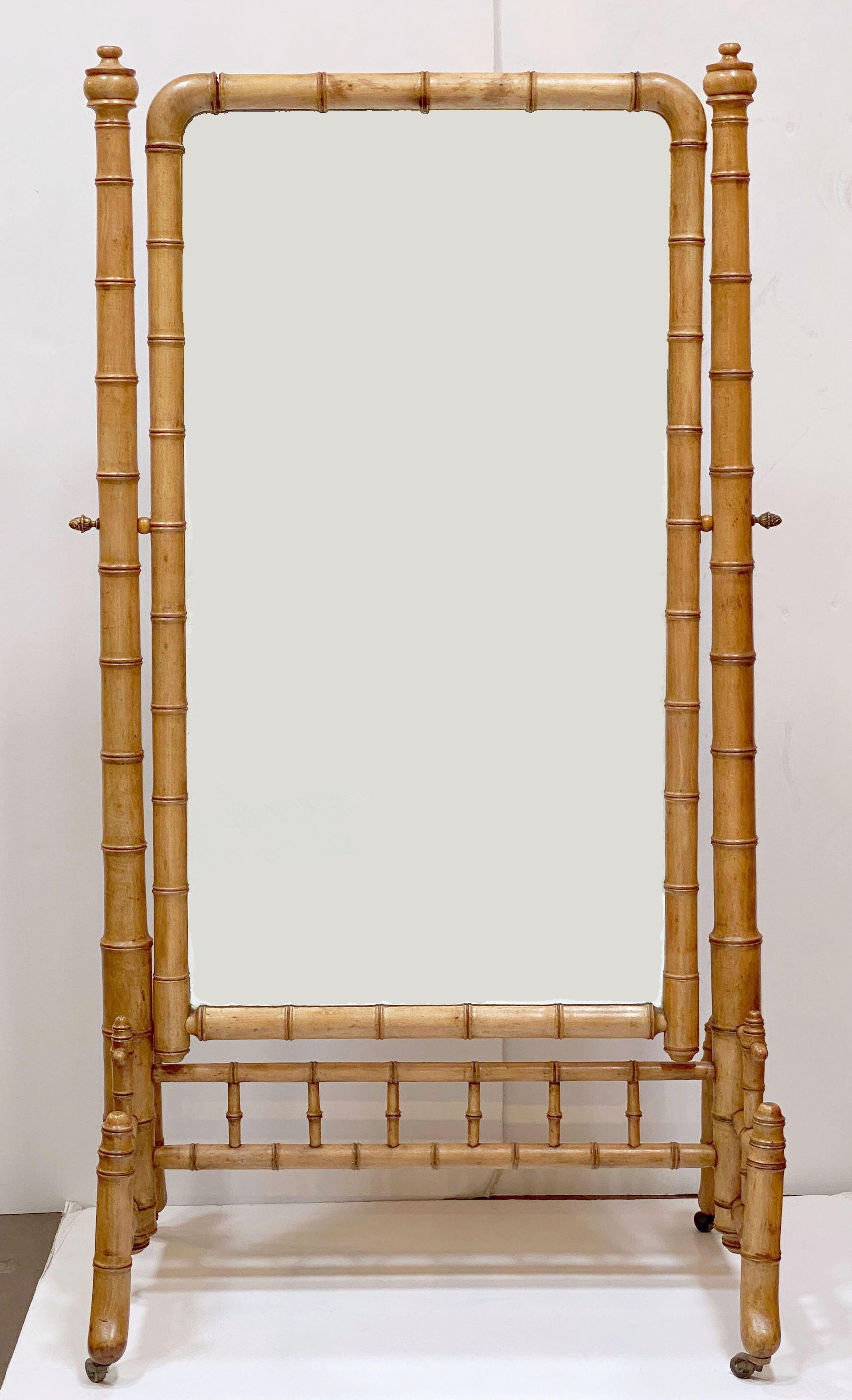 A fine large French faux bamboo cheval or full-length dressing mirror, c.1870-1910, featuring a mirrored glass panel framed in turned wood with a bamboo design, mounted to a rolling frame of turned wood, capped with turned finials, with a stretcher