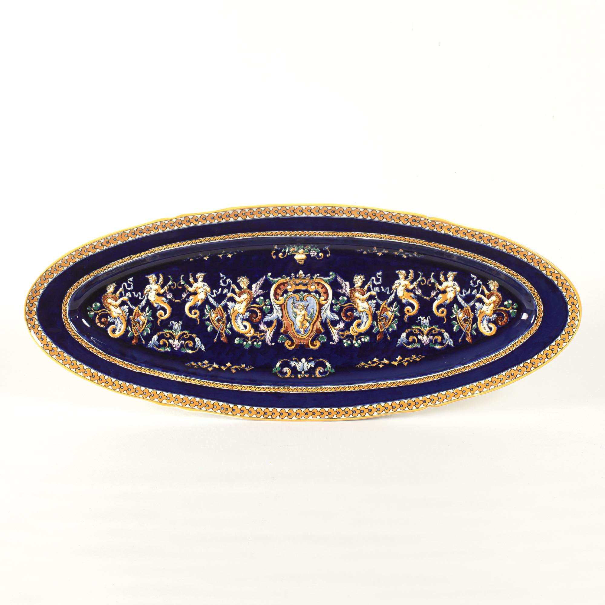 Huge oval serving platter from Gien with cobalt blue background for hand painted grotesque decorations inspired by fifteenth-century Italy.
The motifs in yellow, white and brown highlights depict chimeras, scrolls, bearded men, masks, children.
This