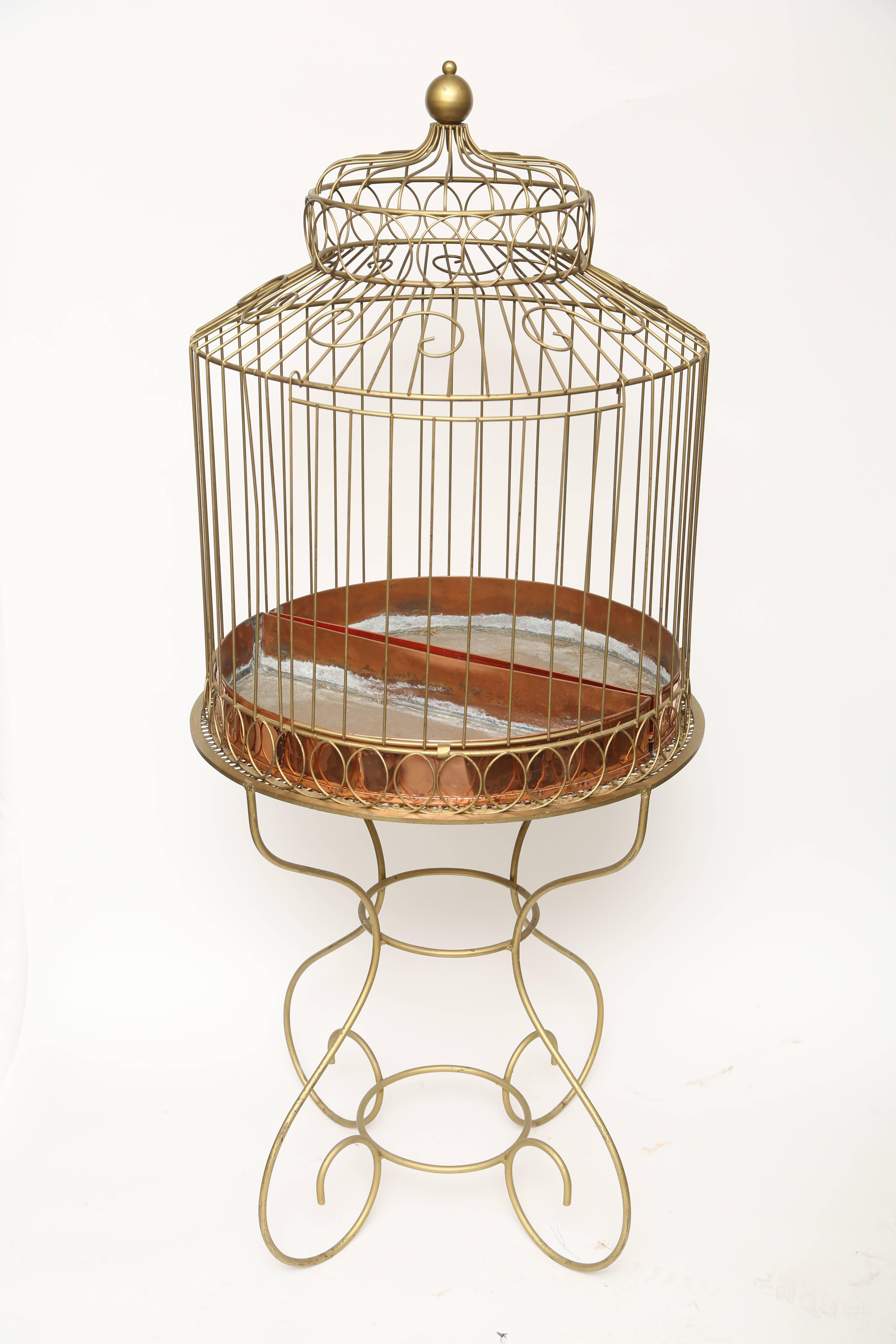 This large custom made two part bird cage has been made of gilt metal with two half round copper inserts to cover the bottom of the cage.. The cage itself has scrolled designs with a large door in the centre front. The base has a pierced top and