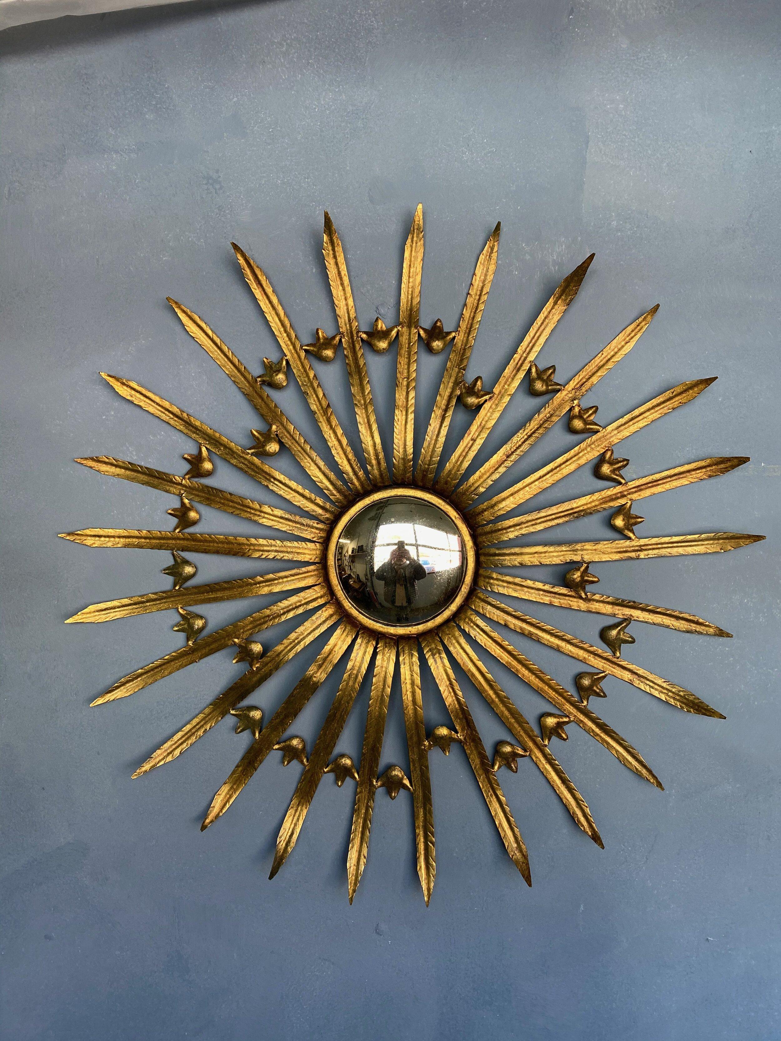 This unique and decorative gilt metal sunburst mirror presents a captivating design. The mirror features pointed rays that are 25 inches long, delicately separated by stylized leaf pattern dividers, creating an intriguing visual effect. The central