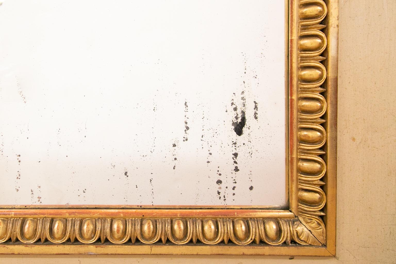 Grand miroir doré français, la couleur de base est crème avec des moulures dorées en forme d'œuf et de fléchette autour du miroir. Les côtés ont des colonnes tournées et anglées avec des feuilles d'acanthe près de la base.
       