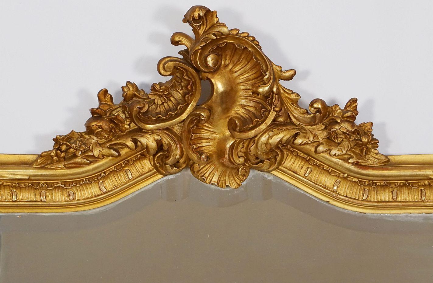 A fine large French giltwood pier or wall mirror from the 19th century, featuring an arched top with Rococo cartouche and foliate flourishes, showing decorative rosettes and scrollwork around the frame and to the base.