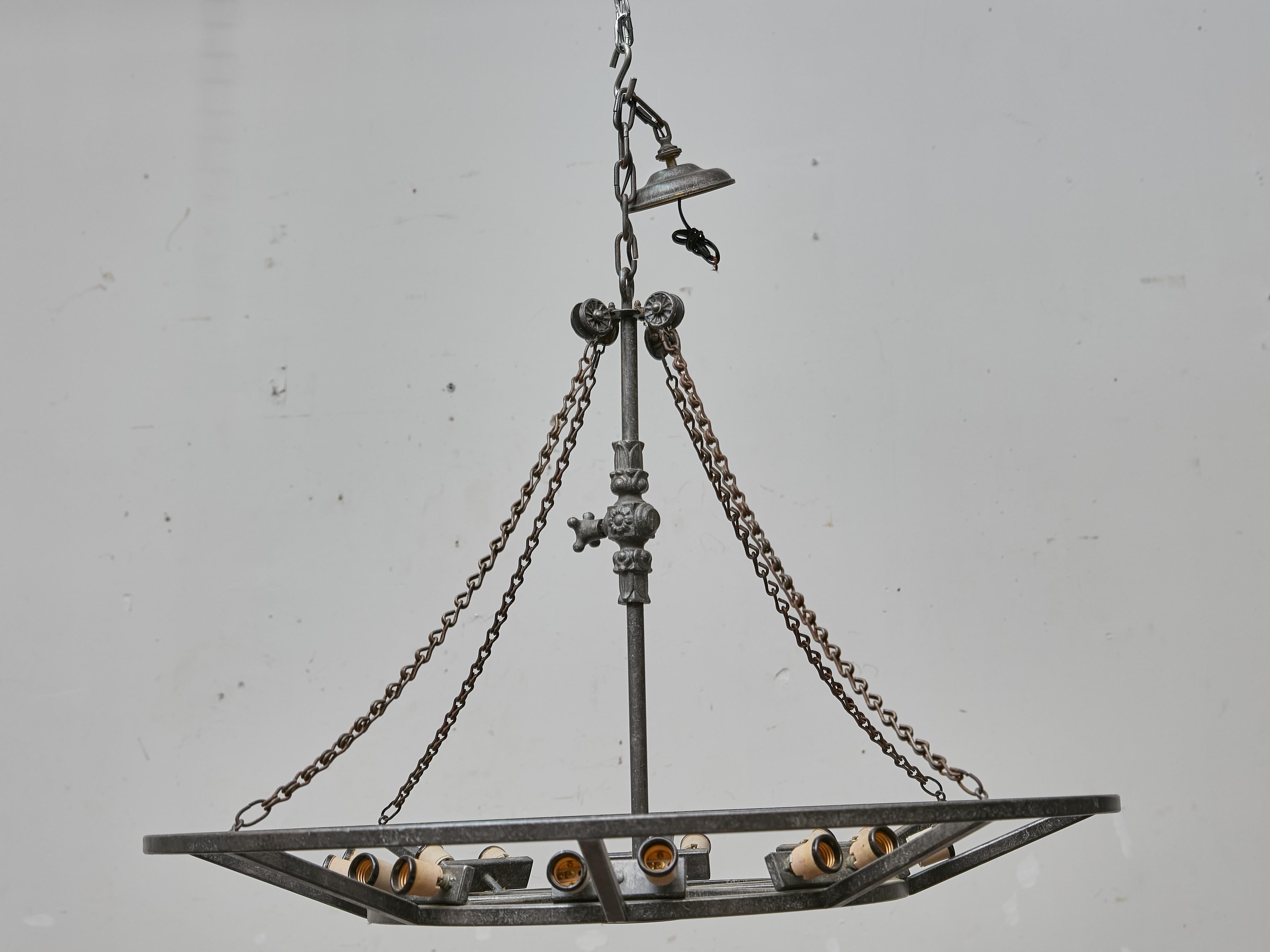 Realizzato in Francia intorno al 1920-1930, questo straordinario lampadario in ferro combina la forza industriale con una raffinata sobrietà decorativa. La struttura circolare, forgiata in ferro battuto, presenta un'audace struttura geometrica