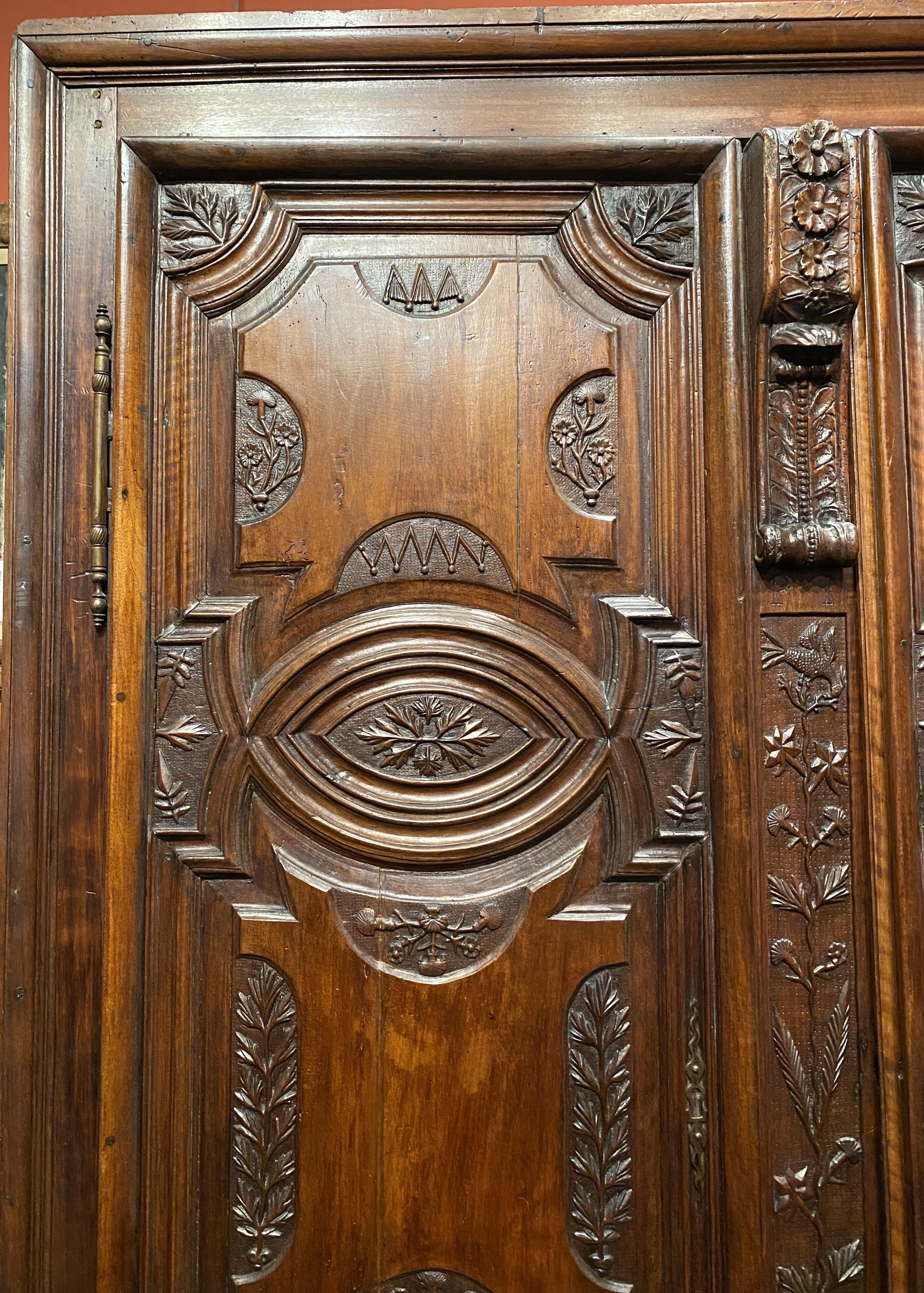 A large French Louis XIV two door walnut cabinet with impressive foliate hand carved front door panels, original brass door escutcheon and hinges, hand carved side panels, original wrought iron door locks on the top and bottom, a heavily restored