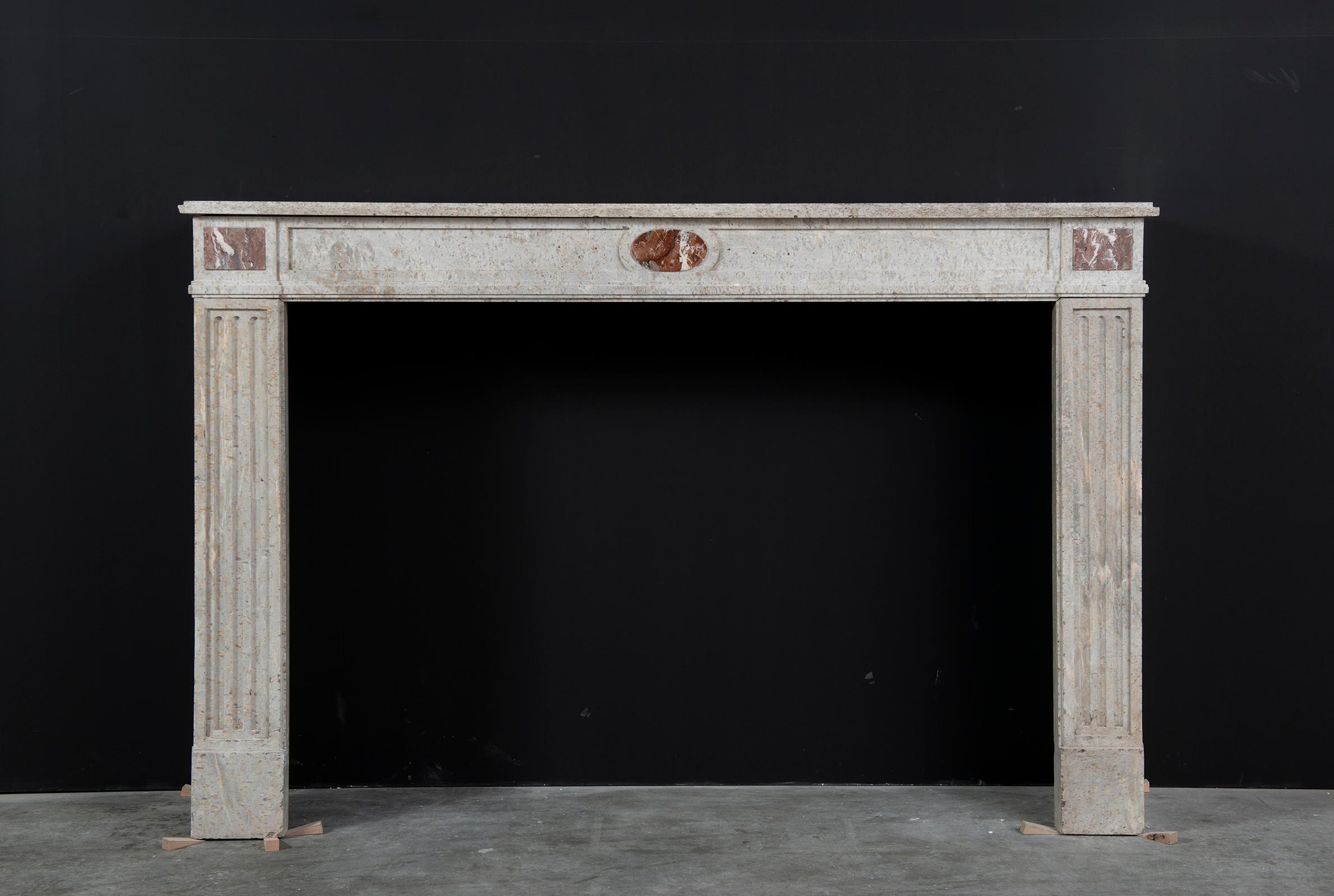 A very nice proportioned beige colored Louis XVI fireplace mantel from France.

Rectangular profiled shelf sit above a panelled frieze centred by a red marble elliptical inlay with on both sides red marble inlayed endblocks, the fluted and paneled